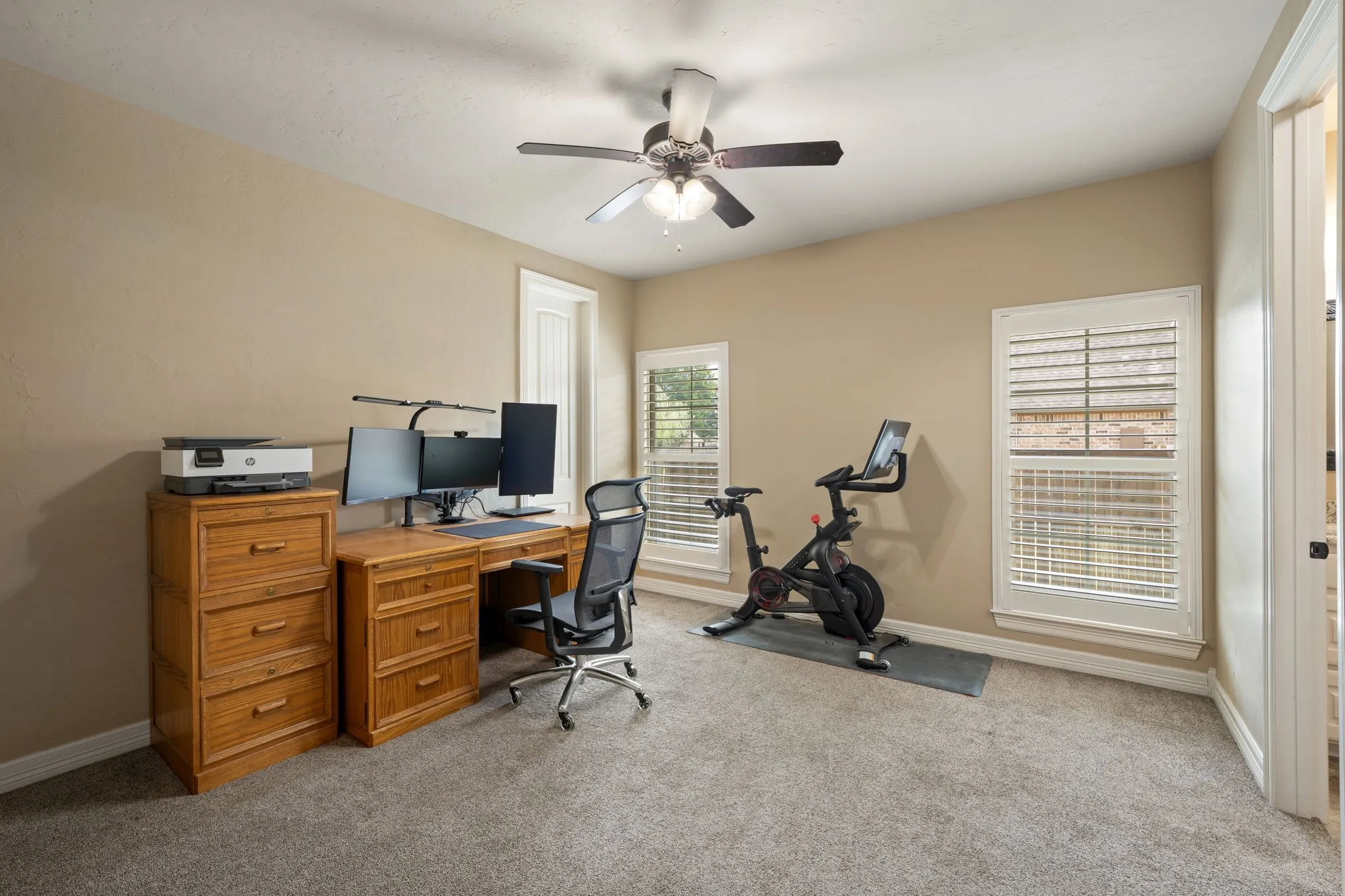 Versatile home office featuring dual wood-finish cabinetry with integrated desk space, ceiling fan with integrated lighting, carpet flooring, and glass French doors providing natural light and access to outdoor spaces