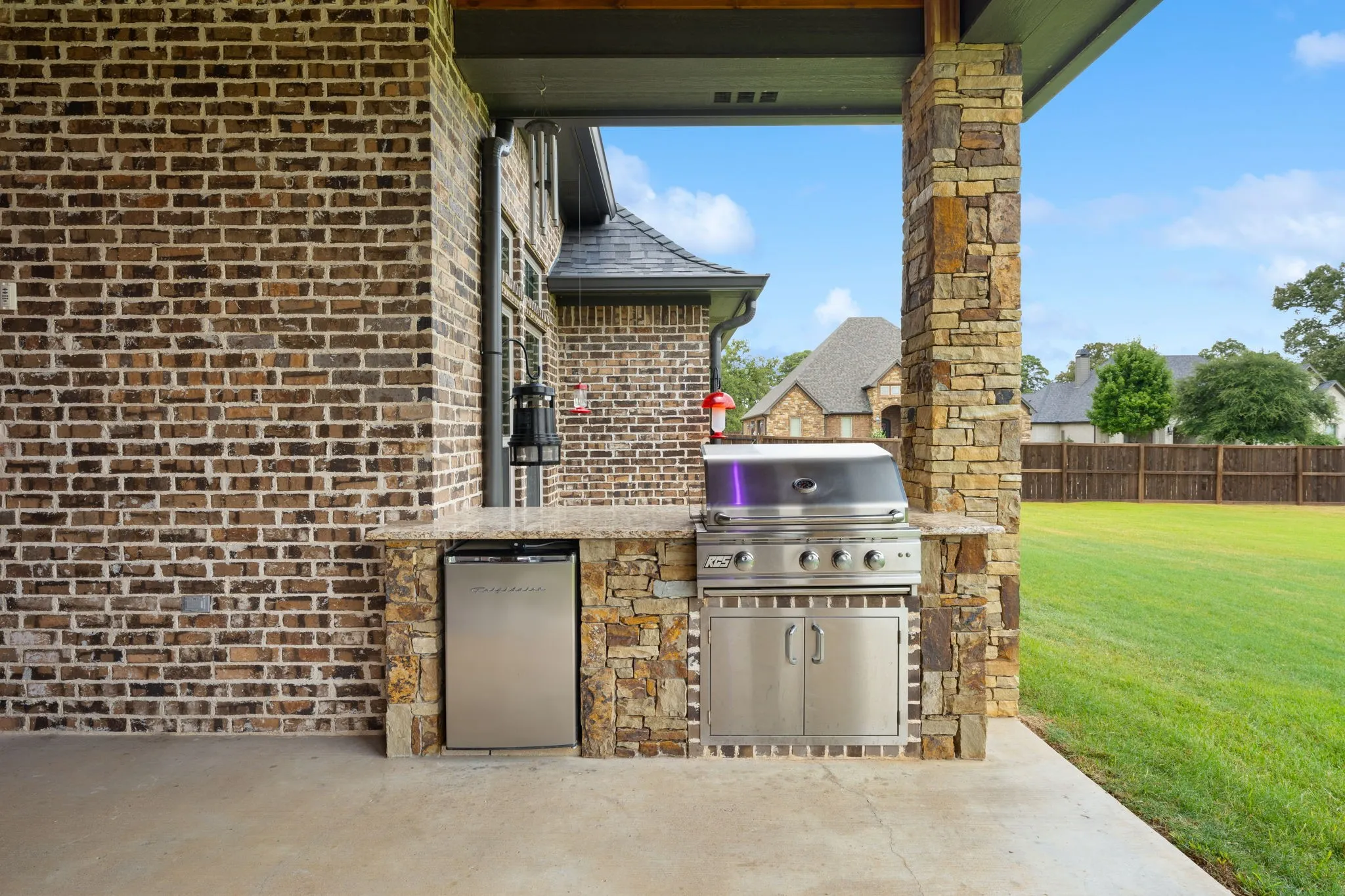 Outdoor kitchen featuring a built-in stainless steel grill, beverage refrigerator, stone-clad base, and a countertop
