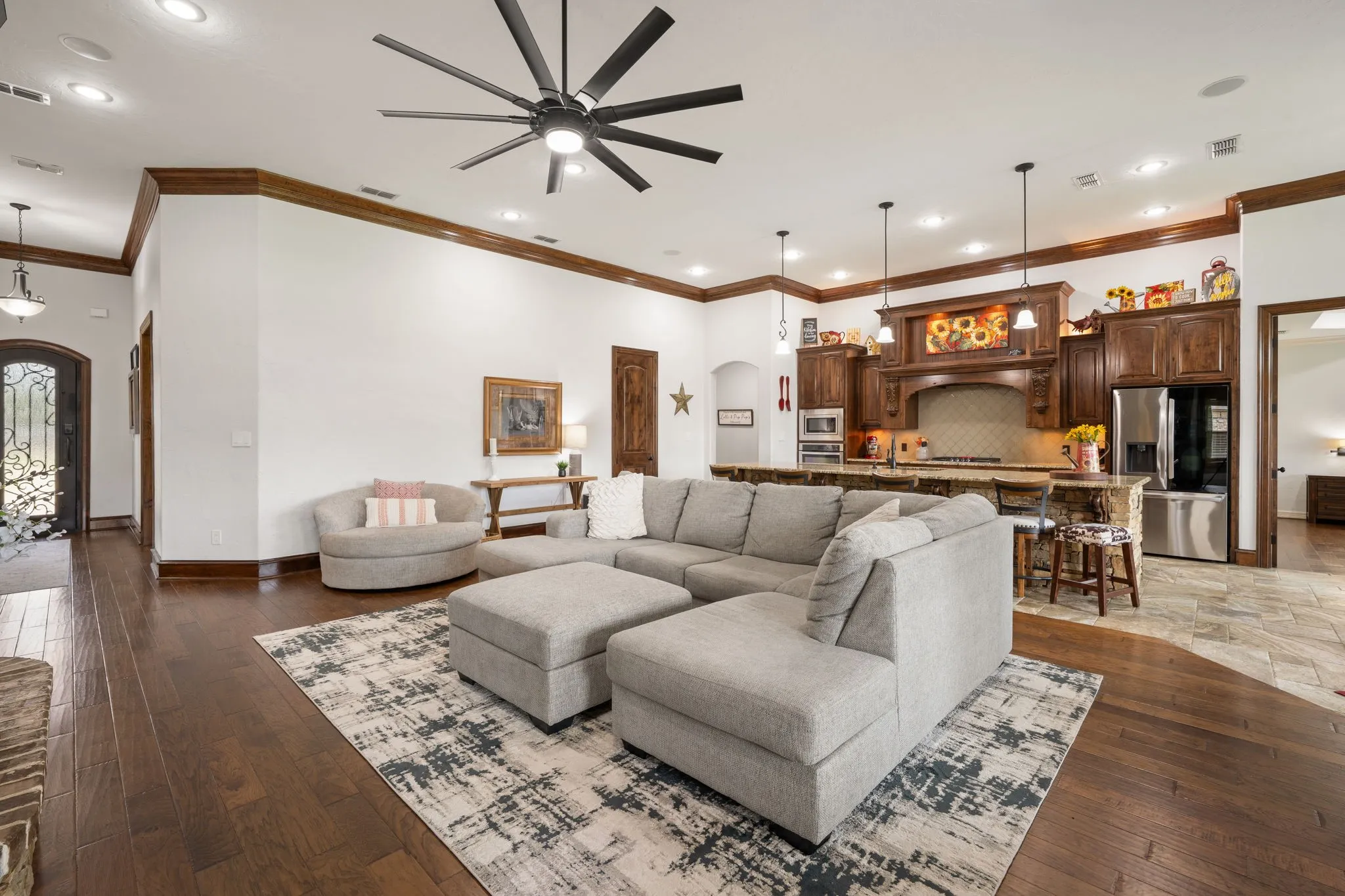 Open-concept living area featuring a large sectional configuration anchored by wood-finish flooring and geometric area rugs