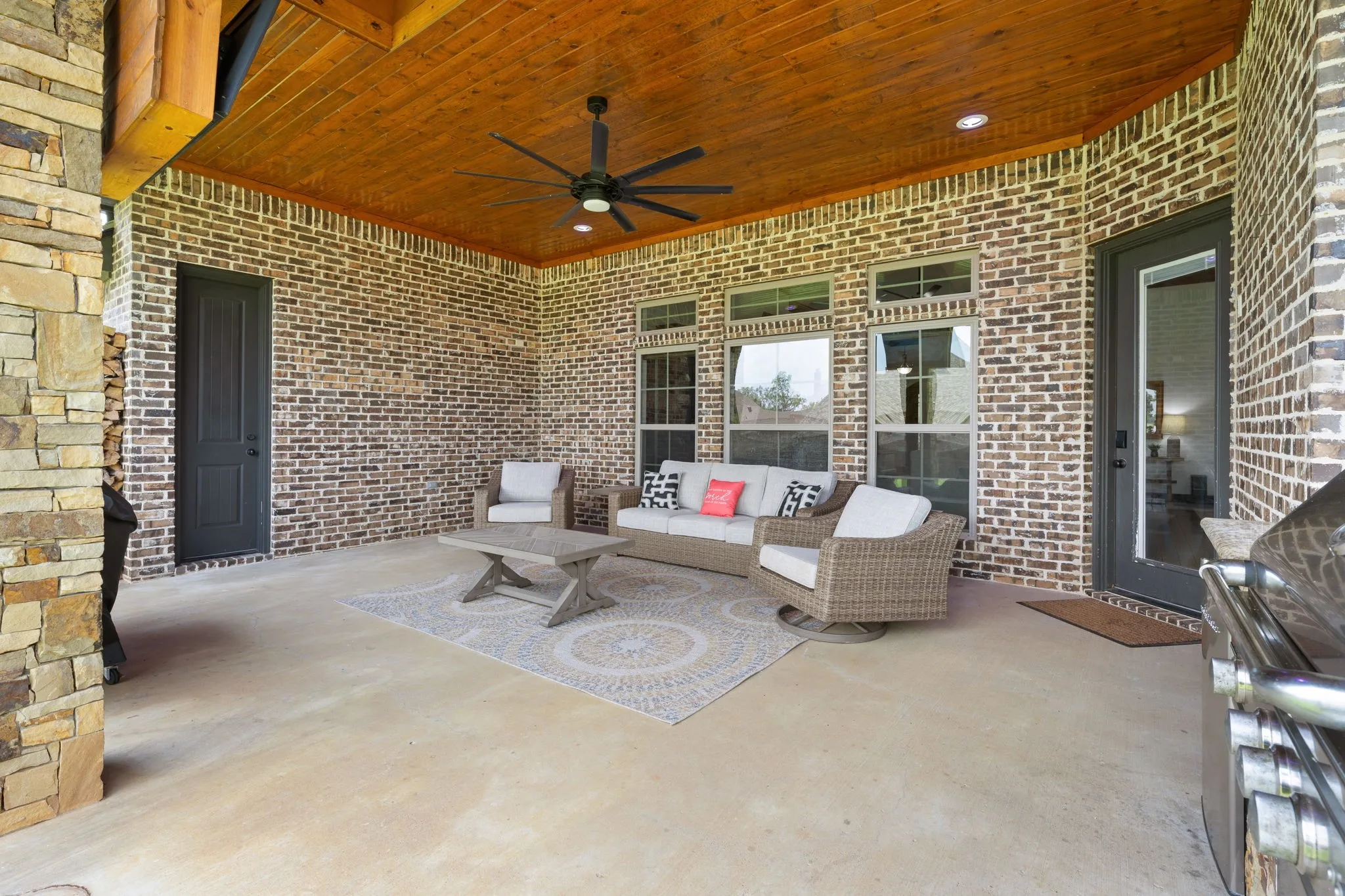 Covered patio featuring brick construction, wood-finish ceiling with ceiling fan, concrete flooring, and multiple glass-panel doors providing access to the outdoor living space