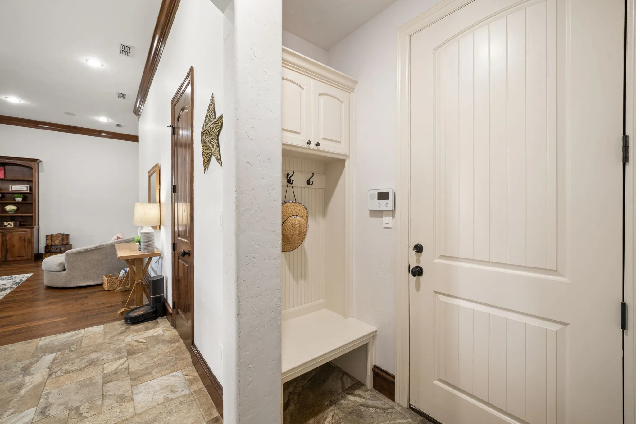 Built-in mudroom bench with upper cabinetry and hooks, panel-style interior door, and multi-toned tile flooring