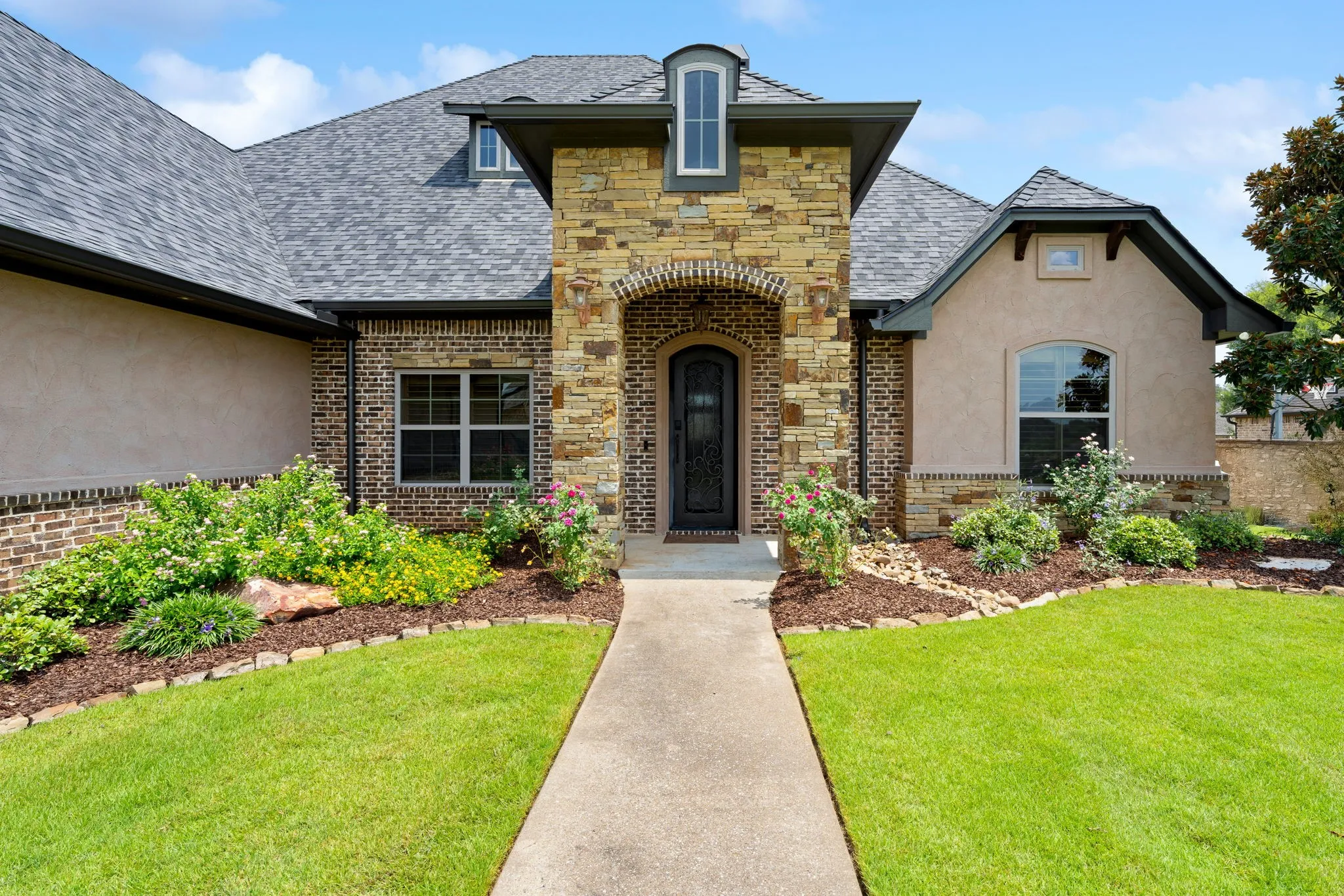 Stone and brick exterior with stucco accents, arched entryway, and mature landscaping