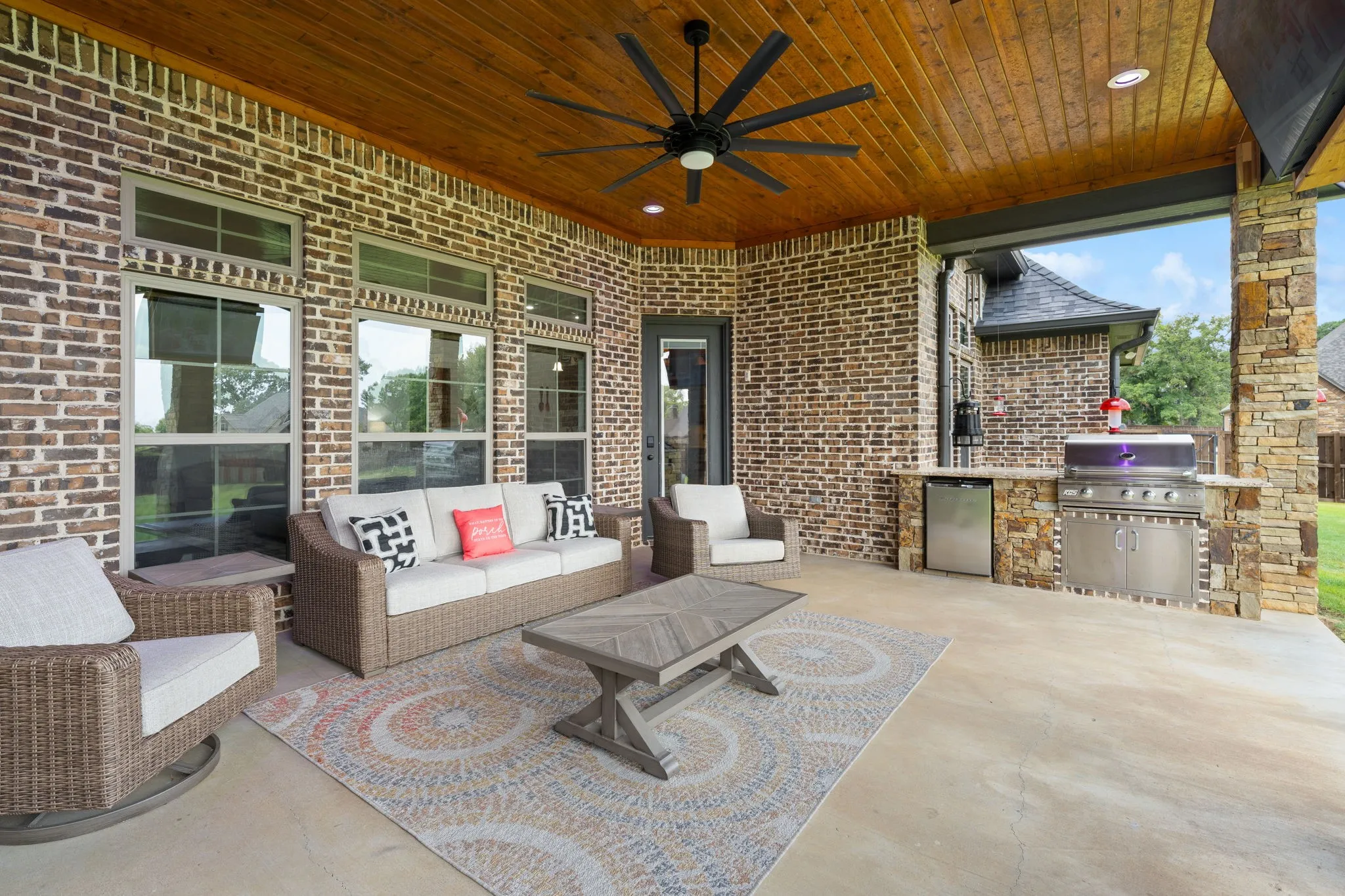 Expansive covered patio featuring a wood-finish ceiling, built-in outdoor kitchen with stainless steel appliances, brick exterior, and a ceiling fan