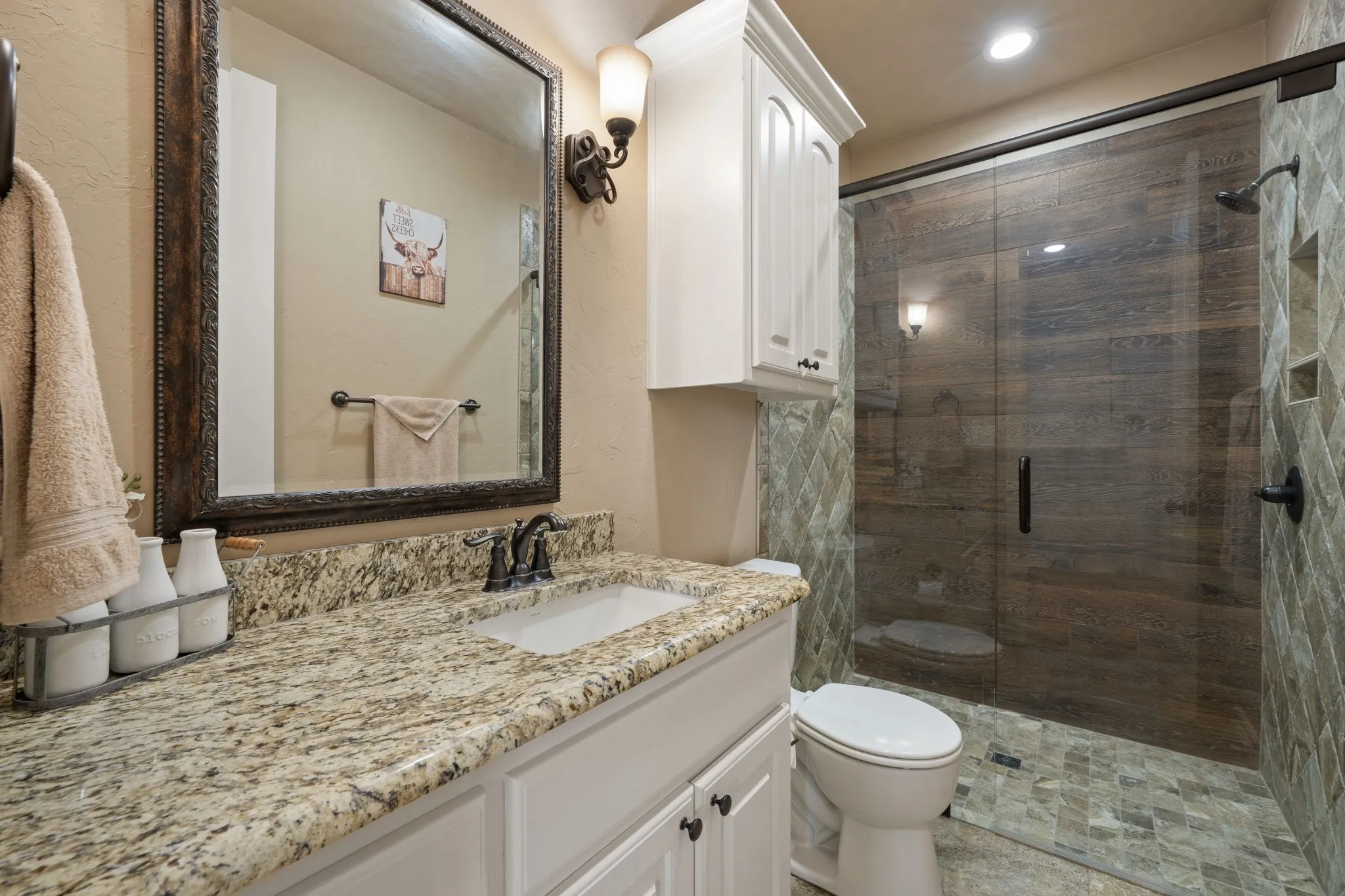 Spa-inspired primary bathroom featuring a spacious walk-in shower with stone-look tile surround and frameless glass enclosure, granite-finish countertop with dual sink vanity, white cabinetry with ample storage, and brushed nickel fixtures throughout