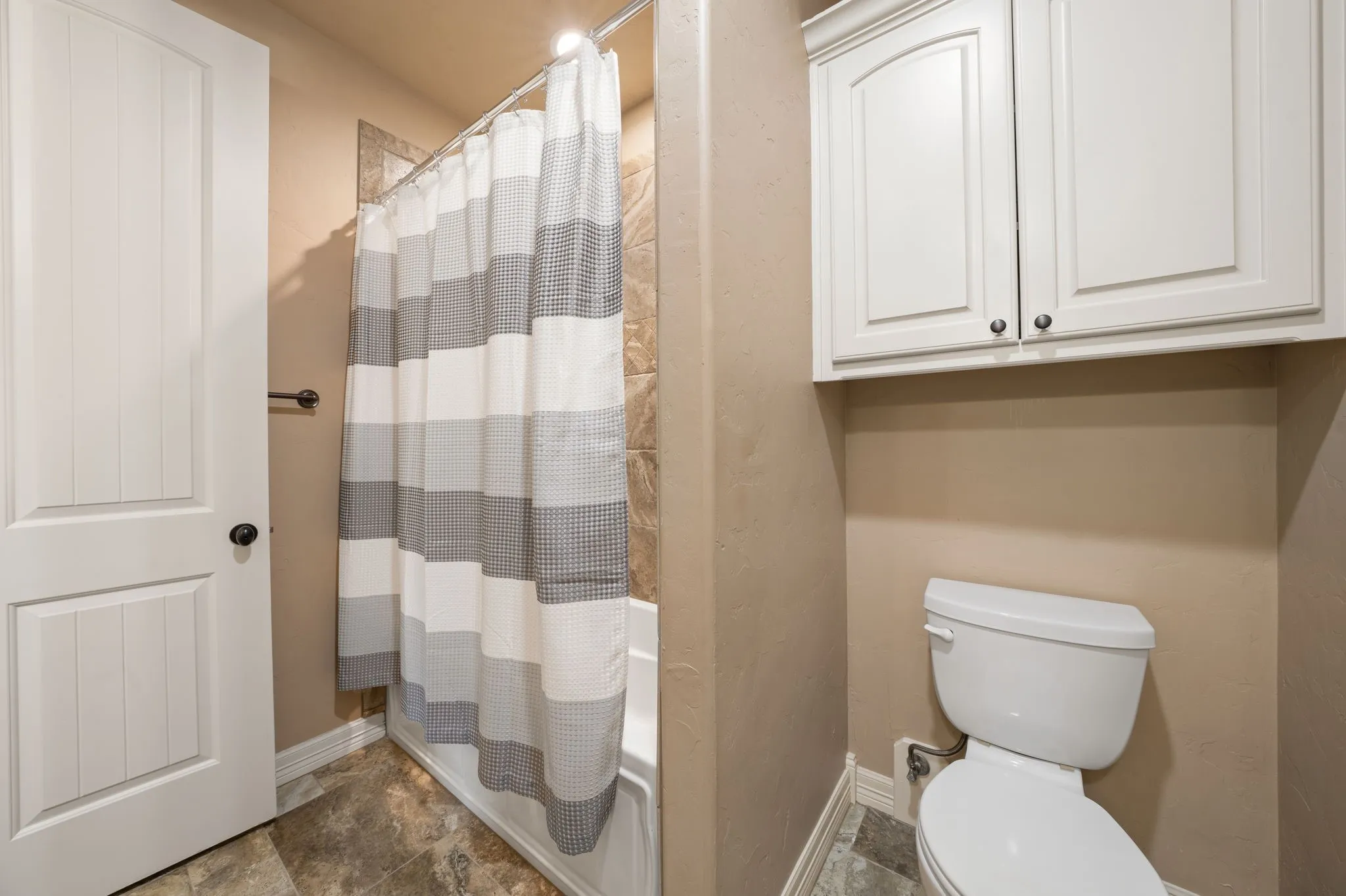 Functional bathroom featuring ceramic tile flooring, a striped shower curtain rod enclosure, white cabinetry with dual doors, and a standard toilet with tank-style design