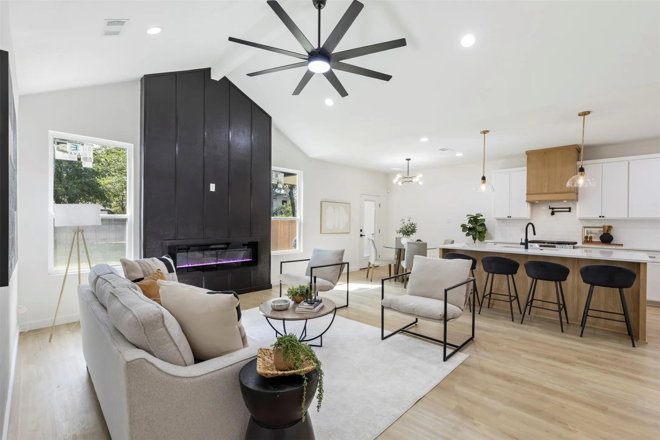 Open-concept living area featuring a wood-finish plank floor, contemporary ceiling fan with integrated lighting, and a gas fireplace with black surround