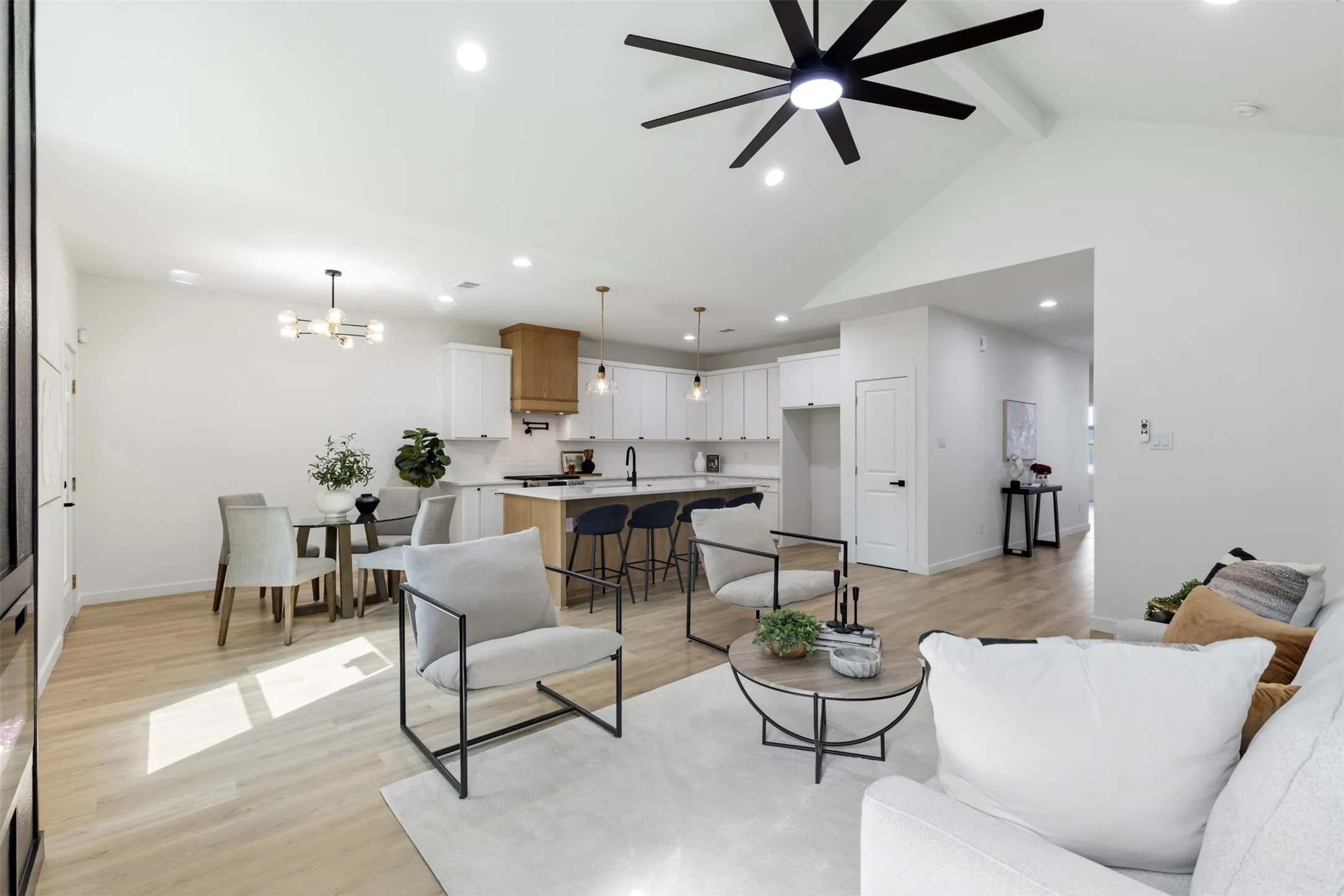 Open-concept living area featuring hardwood flooring, modern black spoke ceiling fan, and abundant natural light