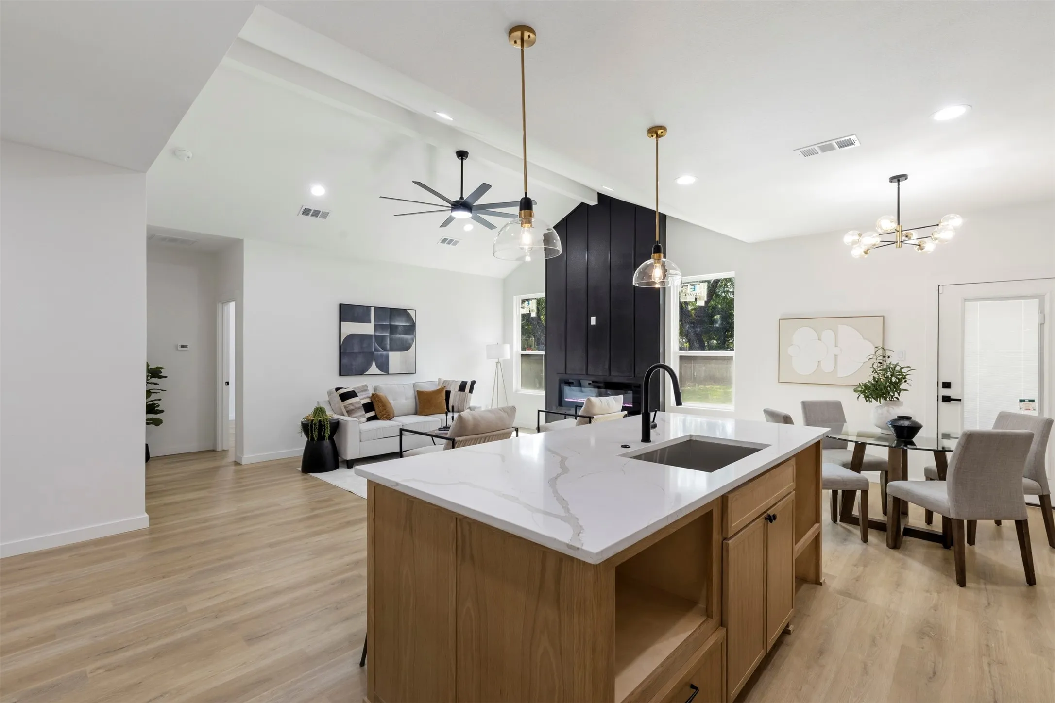 Open-concept kitchen and dining area featuring a wood-finish island with white quartz countertop and integrated sink, wide-plank wood-finish flooring throughout, recessed and pendant lighting, and expansive sightlines to the living spaces