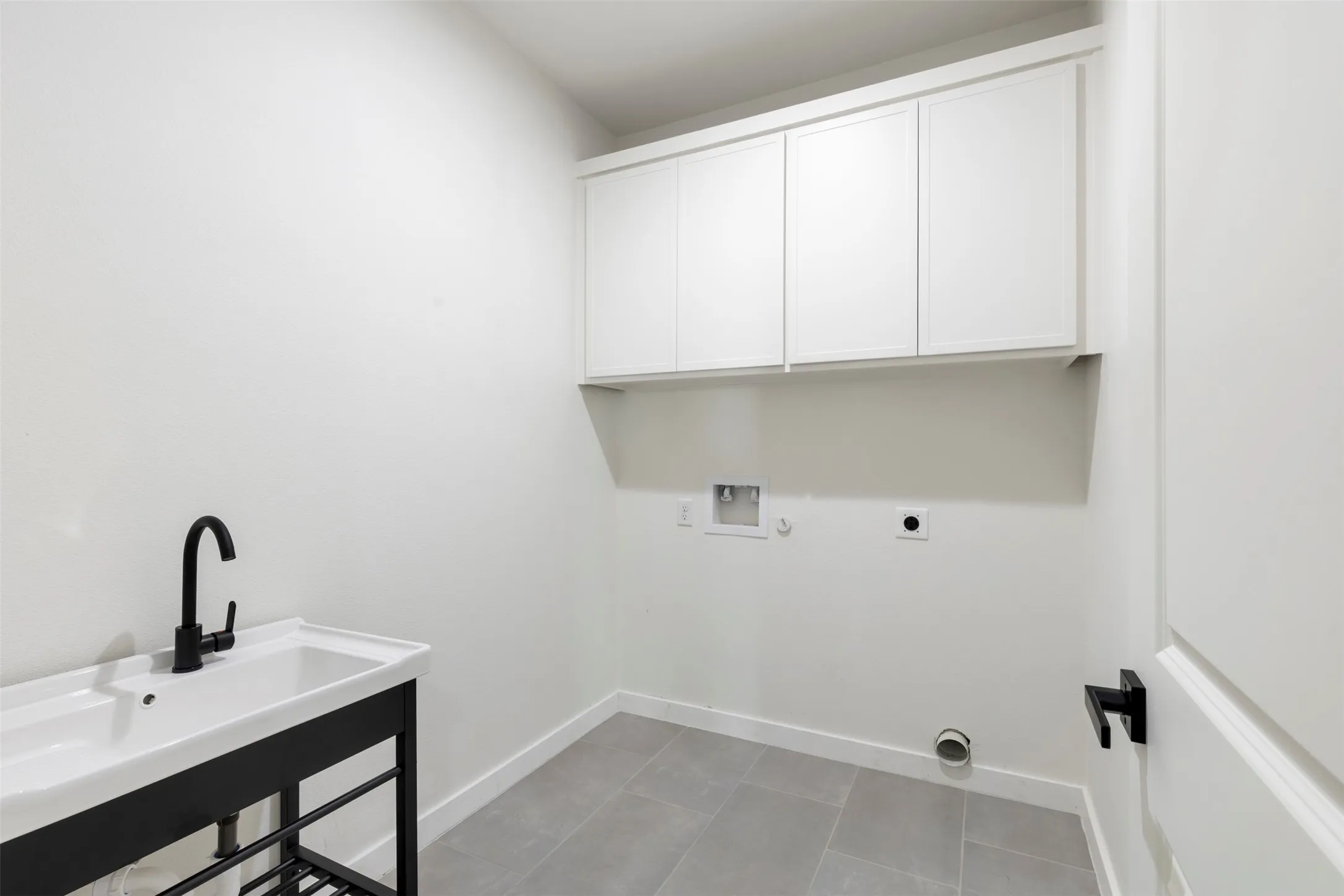 Modern utility room featuring white cabinetry with ample storage, a black matte faucet with contemporary styling, white quartz countertop with integrated sink, gray tile flooring, and recessed lighting throughout
