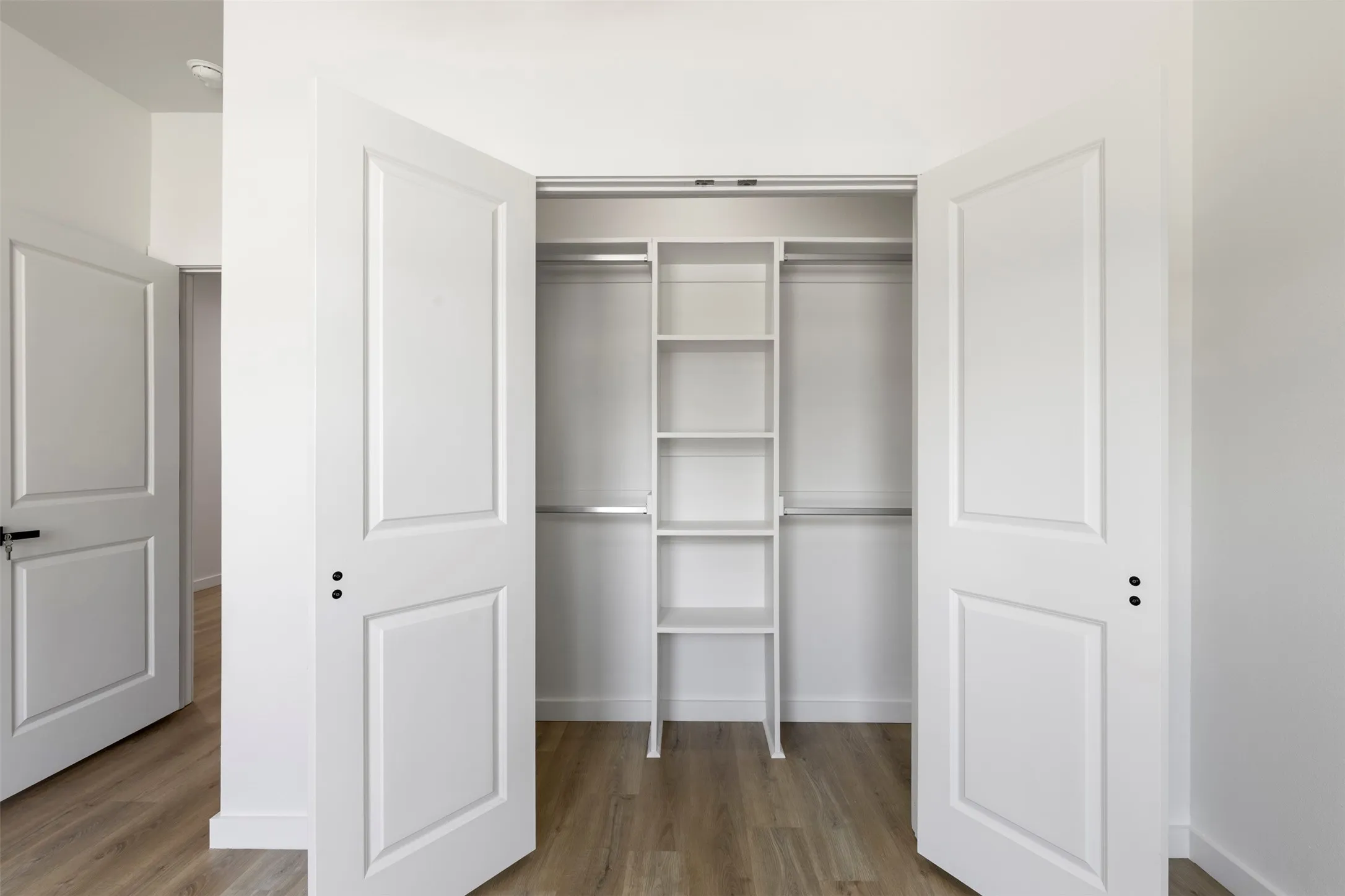 White interior doors with black hardware, built-in closet shelving, and light wood-finish flooring