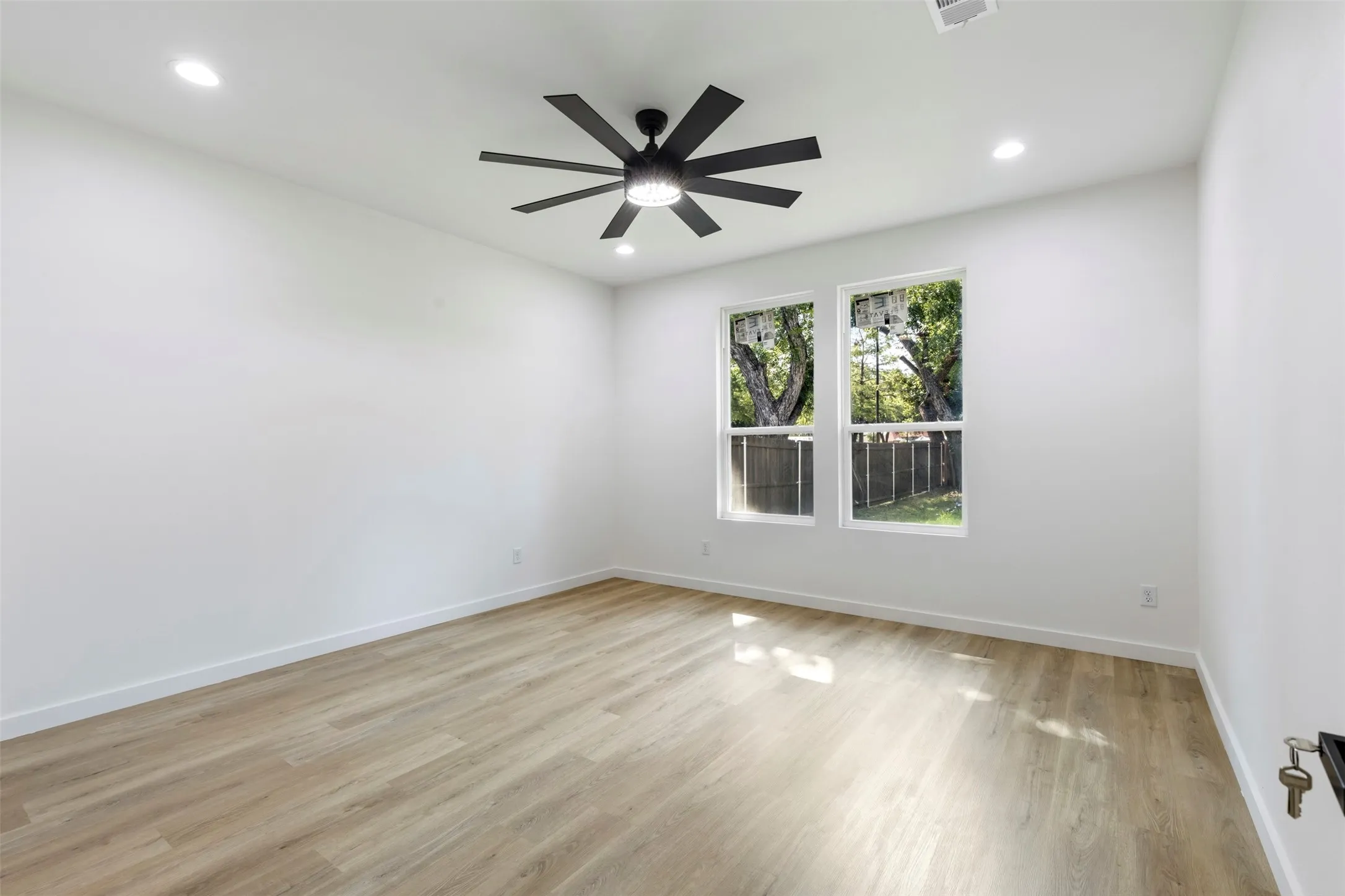 Bright, light-filled room featuring gleaming wood-finish flooring, recessed ceiling lighting, and dual windows framed with black trim that flood the space with natural light