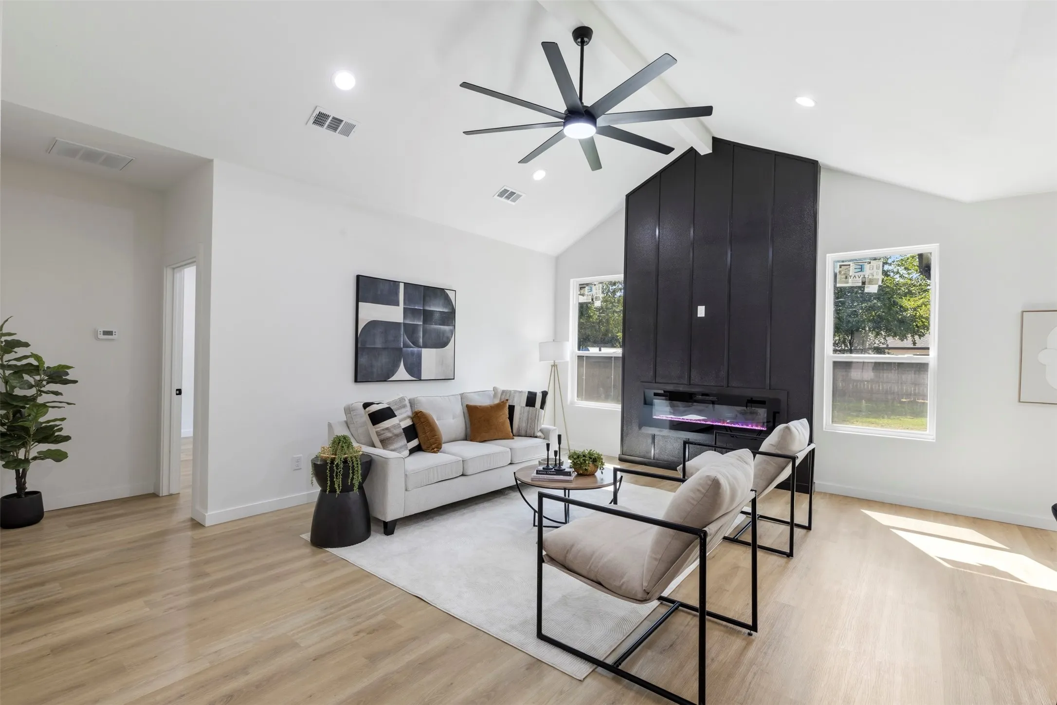 Vaulted ceiling with an attached ceiling fan, recessed lighting, wood-finish flooring, and a floor-to-ceiling fireplace with an electric insert