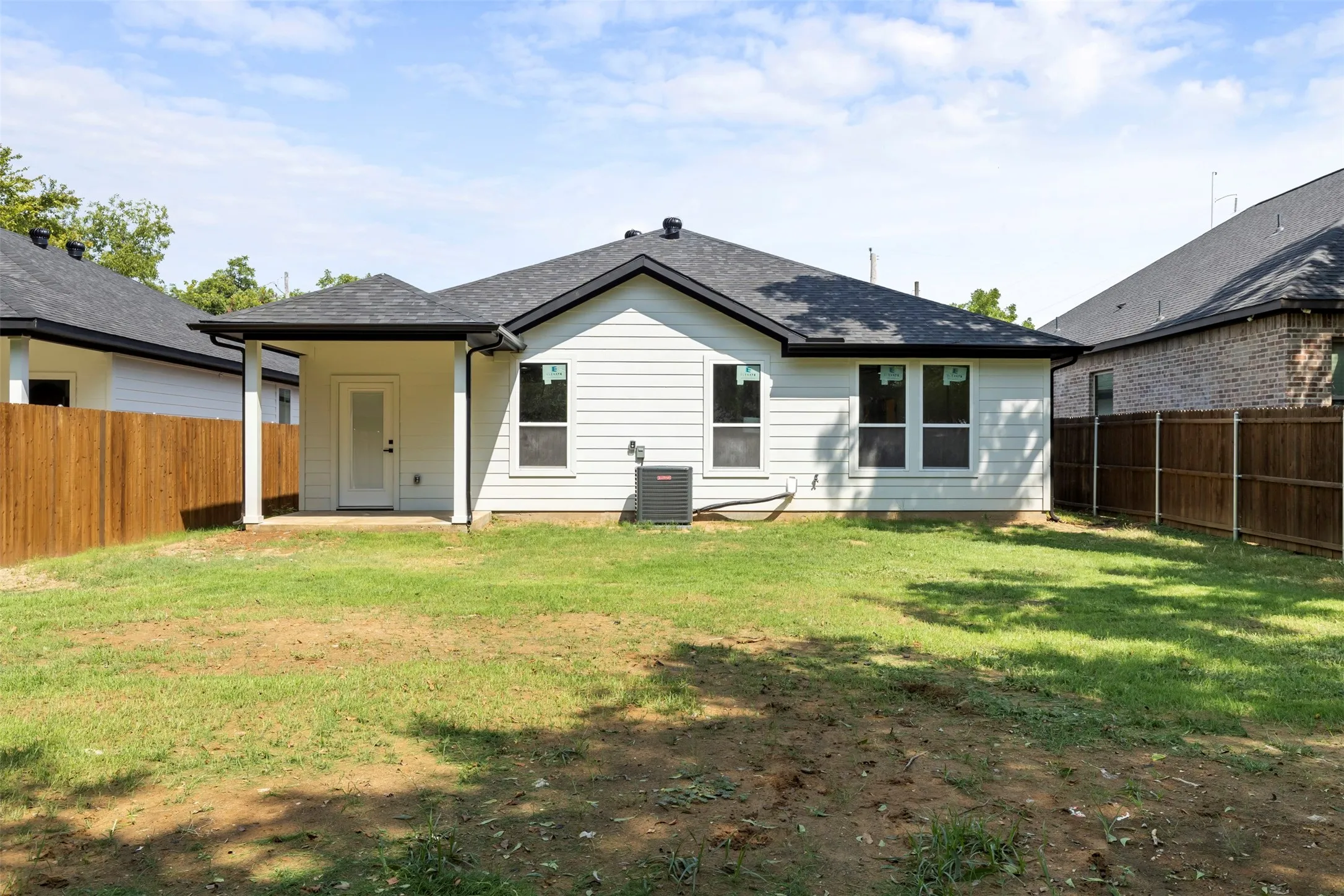 Charming single-story residence featuring a white exterior with black-trimmed windows, covered front porch entry, and an expansive rear yard with mature landscaping and established lawn space