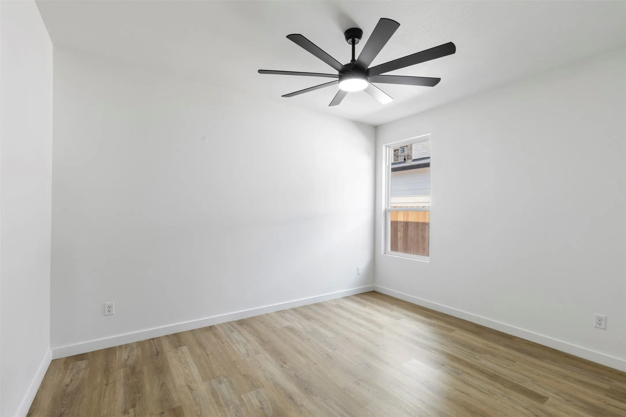 Bright, open bedroom showcasing pristine white walls, warm wood-finish flooring, and abundant natural light from large windows
