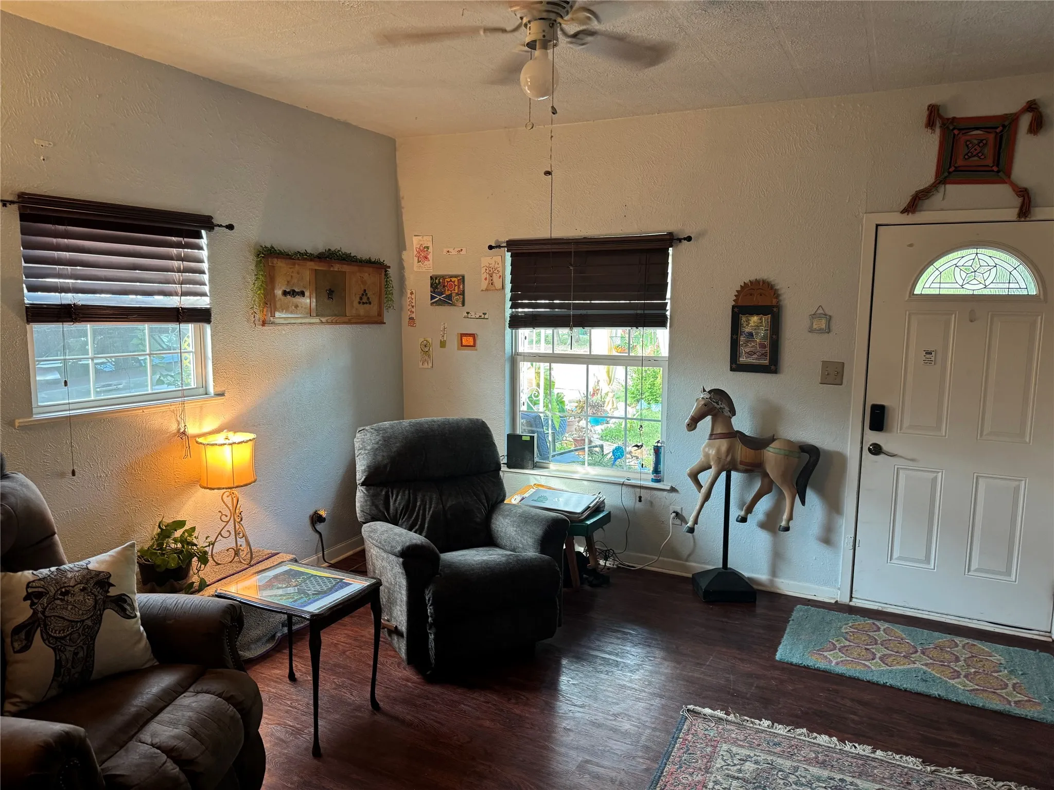 Living area with a textured wall, wood finished floors, healthy amount of natural light, and a ceiling fan
