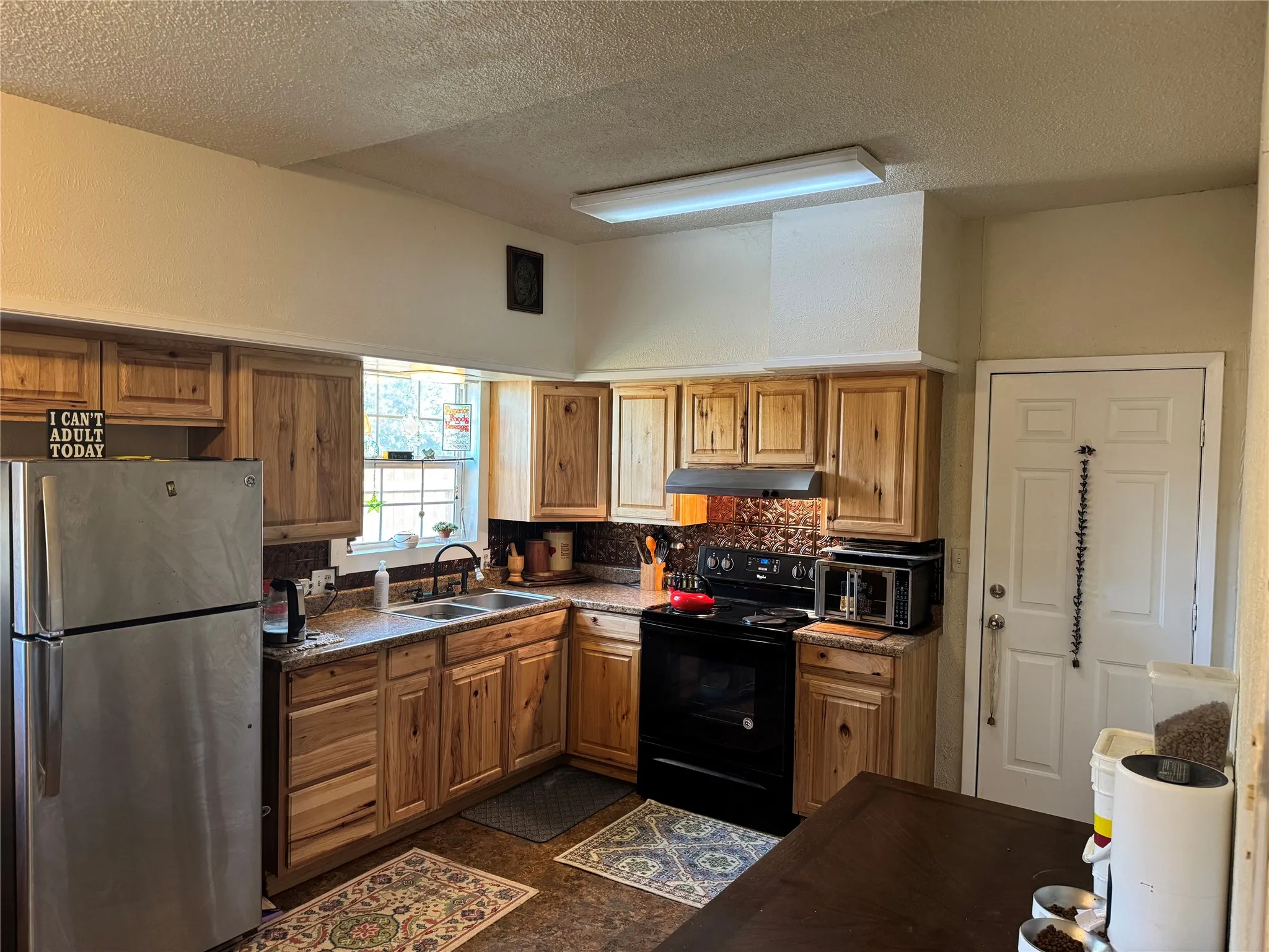 Kitchen featuring freestanding refrigerator, black electric range, brown cabinetry, a textured ceiling, and decorative backsplash