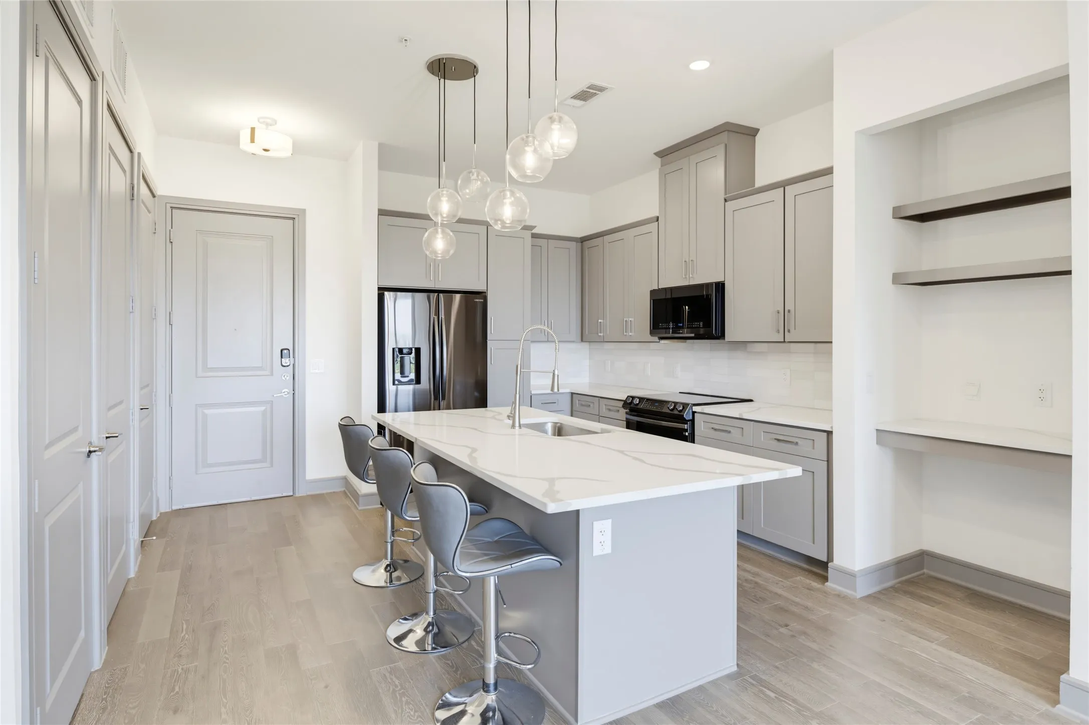 Kitchen featuring a large island with a waterfall countertop, pendant lighting, stainless steel appliances, and wood-finish flooring