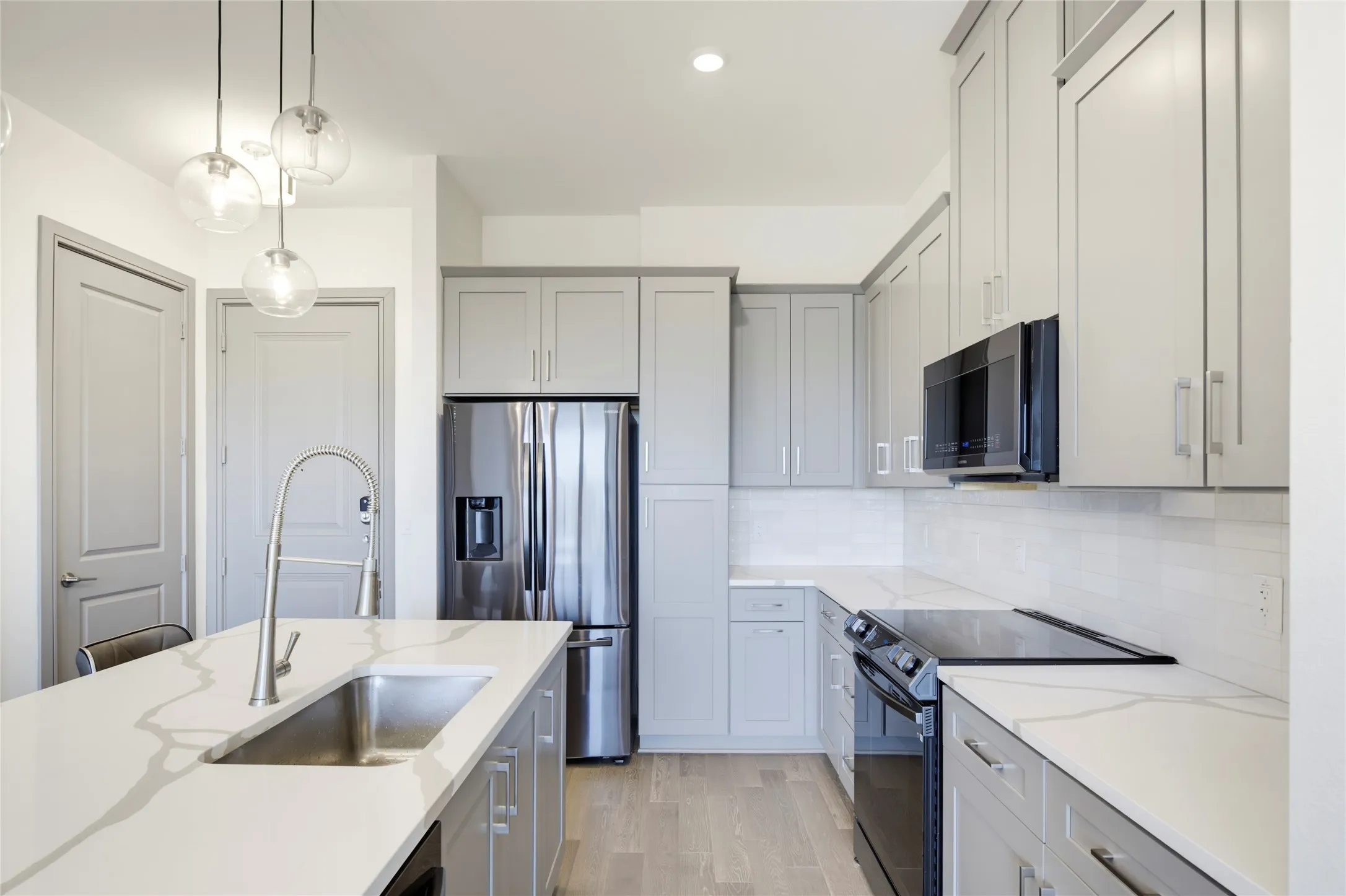 Kitchen featuring light gray cabinetry, stainless steel appliances, white countertops, and wood-finish flooring