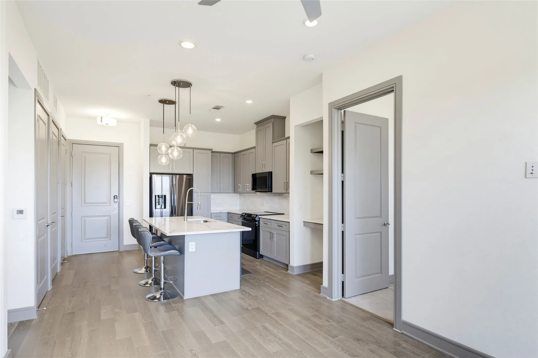 Open-concept kitchen with a central island, grey cabinetry, stainless steel appliances, and wood-finish flooring