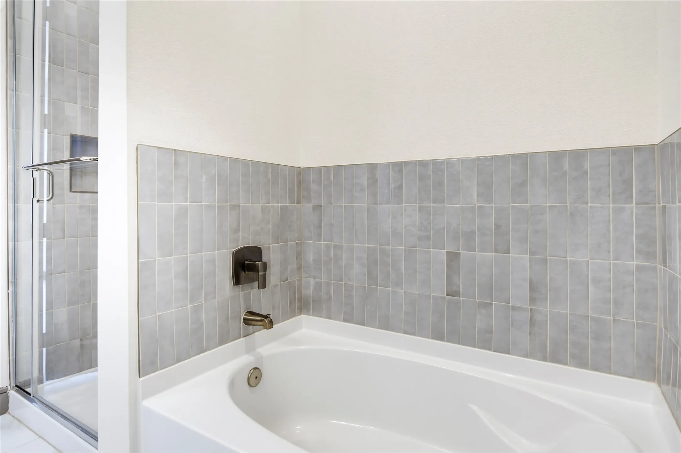 Integrated soaking tub with gray tile surround, oil-rubbed bronze fixtures, and a glass-enclosed shower with matching gray tile