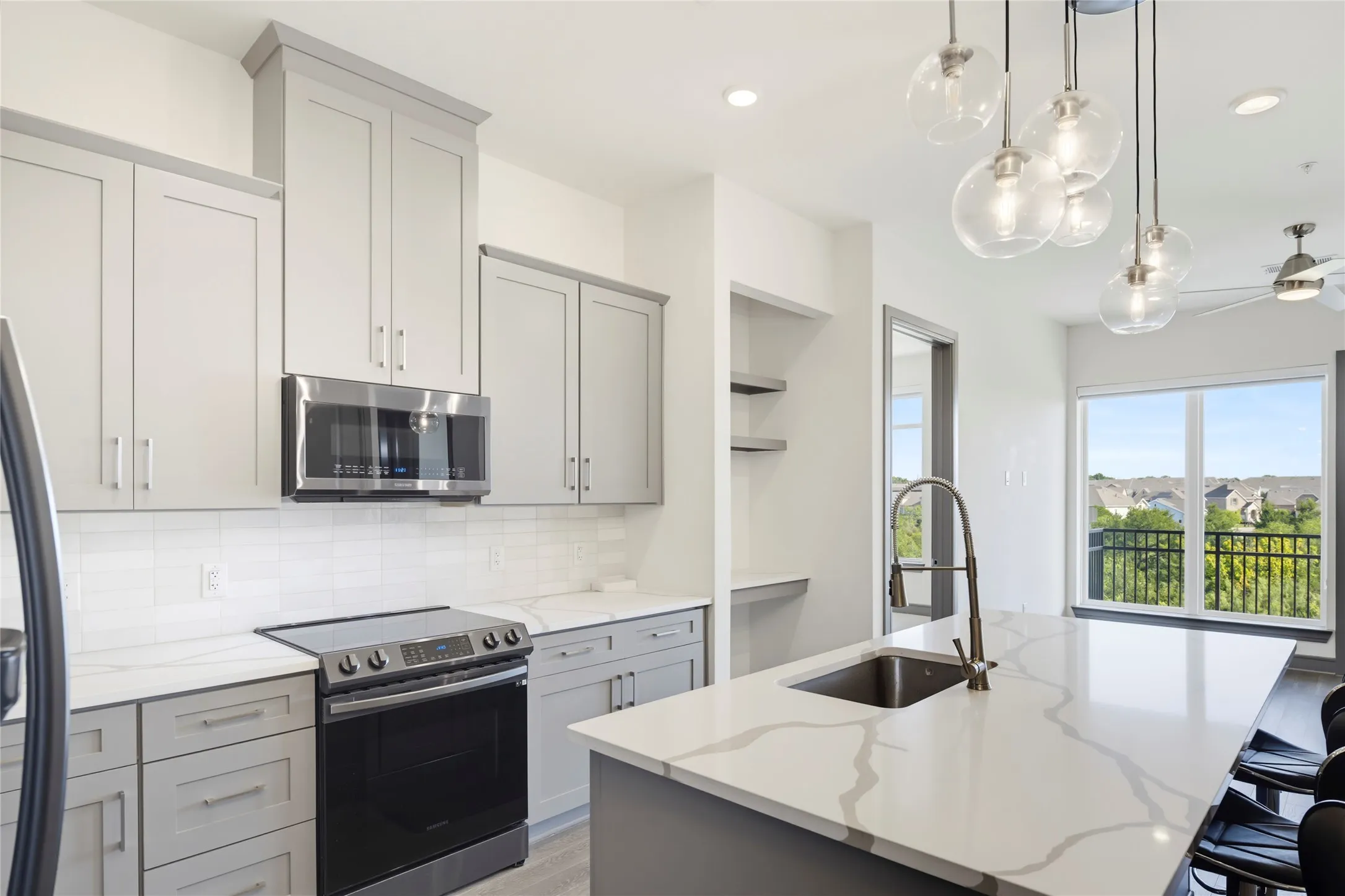 Kitchen featuring gray cabinetry, stainless steel appliances, a subway tile backsplash, and a large island with an undermount sink