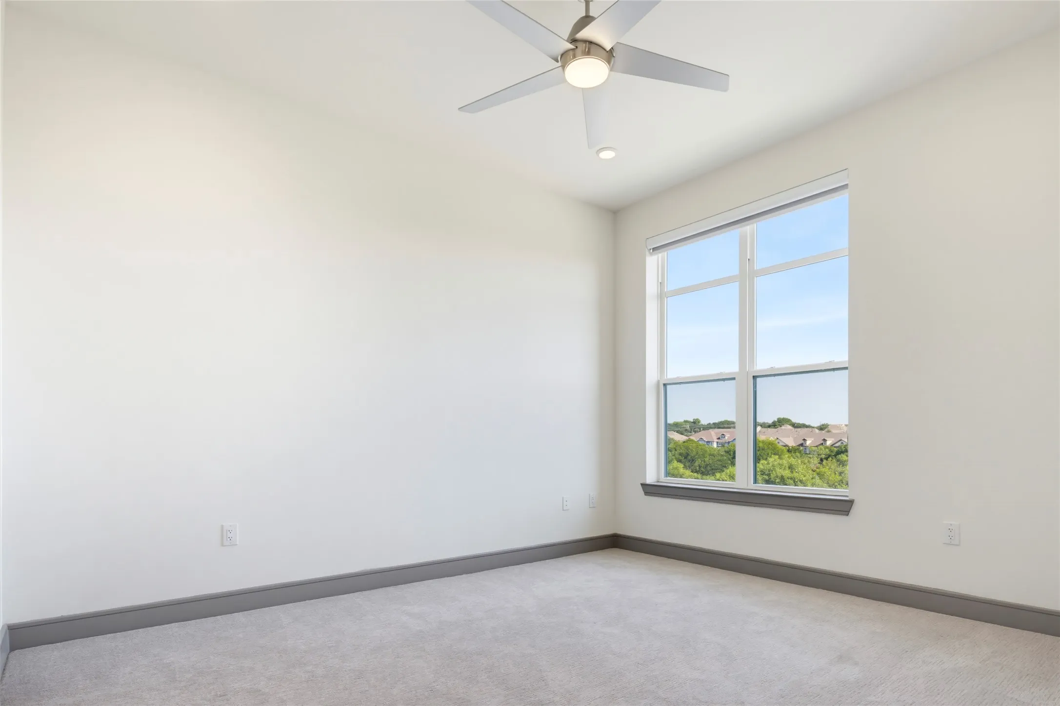 Neutral carpeted flooring, large window with expansive outdoor scenery, modern ceiling fan with integrated lighting, and neutral wall tones