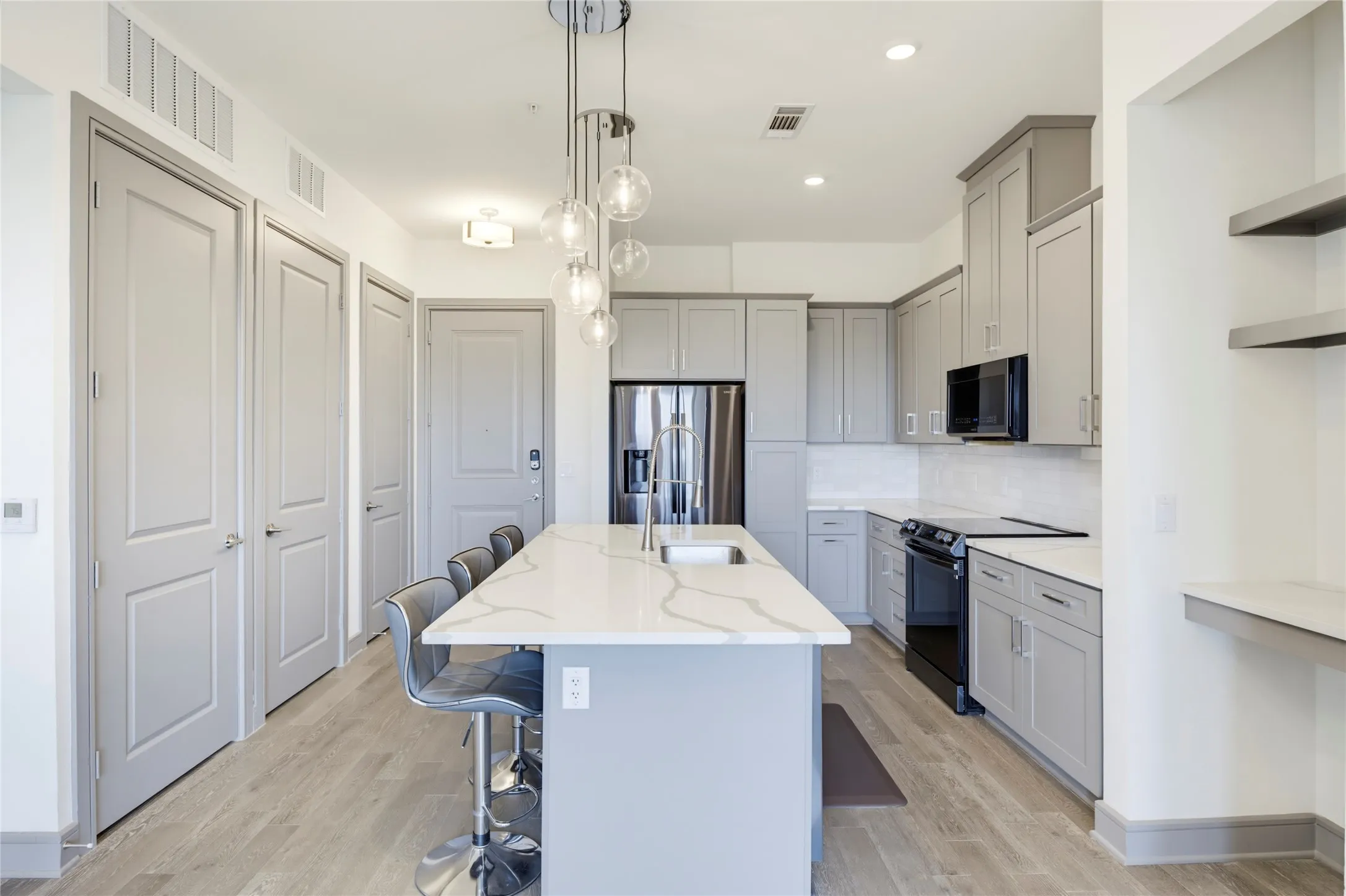 Kitchen featuring a large island with sink, white countertops, gray cabinetry, and stainless steel appliances
