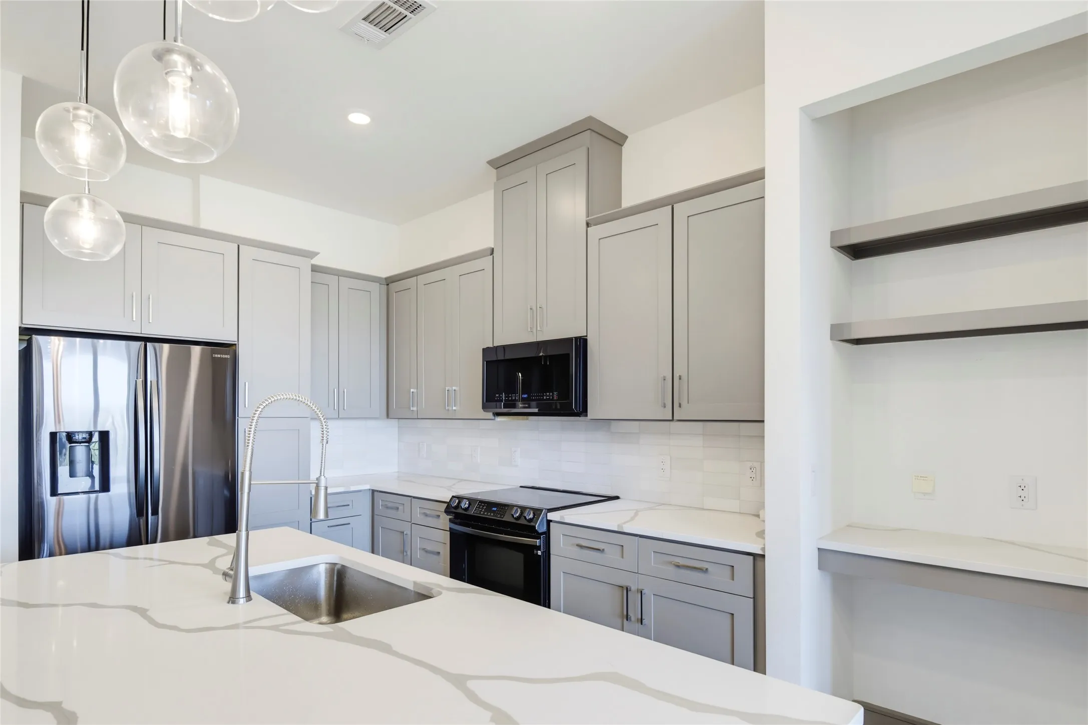 Kitchen featuring light gray cabinetry, white countertops with veining, a stainless steel refrigerator, a black electric range, and a built-in desk area with open shelving