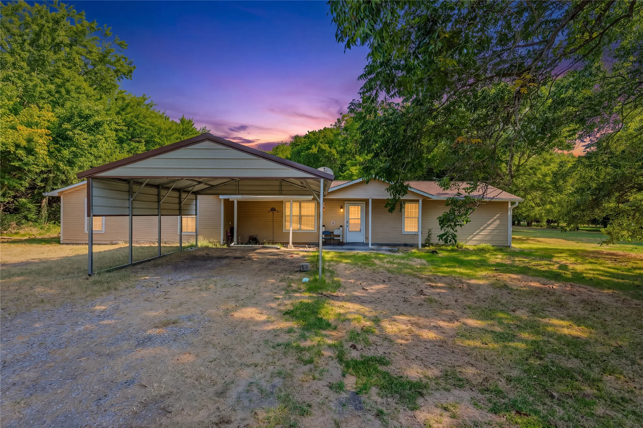 Charming rural residence featuring a carport with metal framework, front-facing covered entry, and illuminated interior spaces
