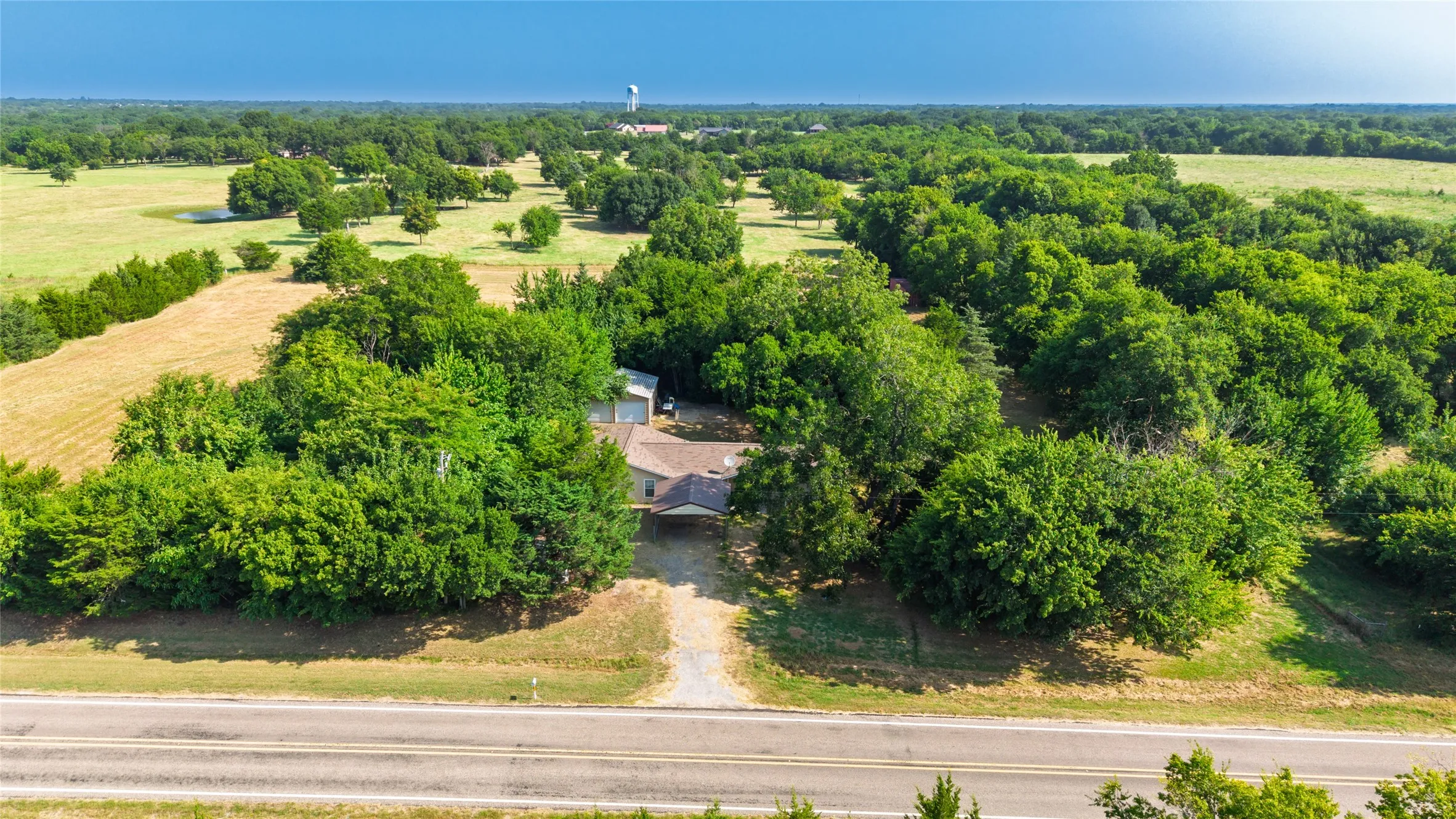 Scenic rural property featuring mature tree-lined grounds, expansive open acreage, and direct highway frontage