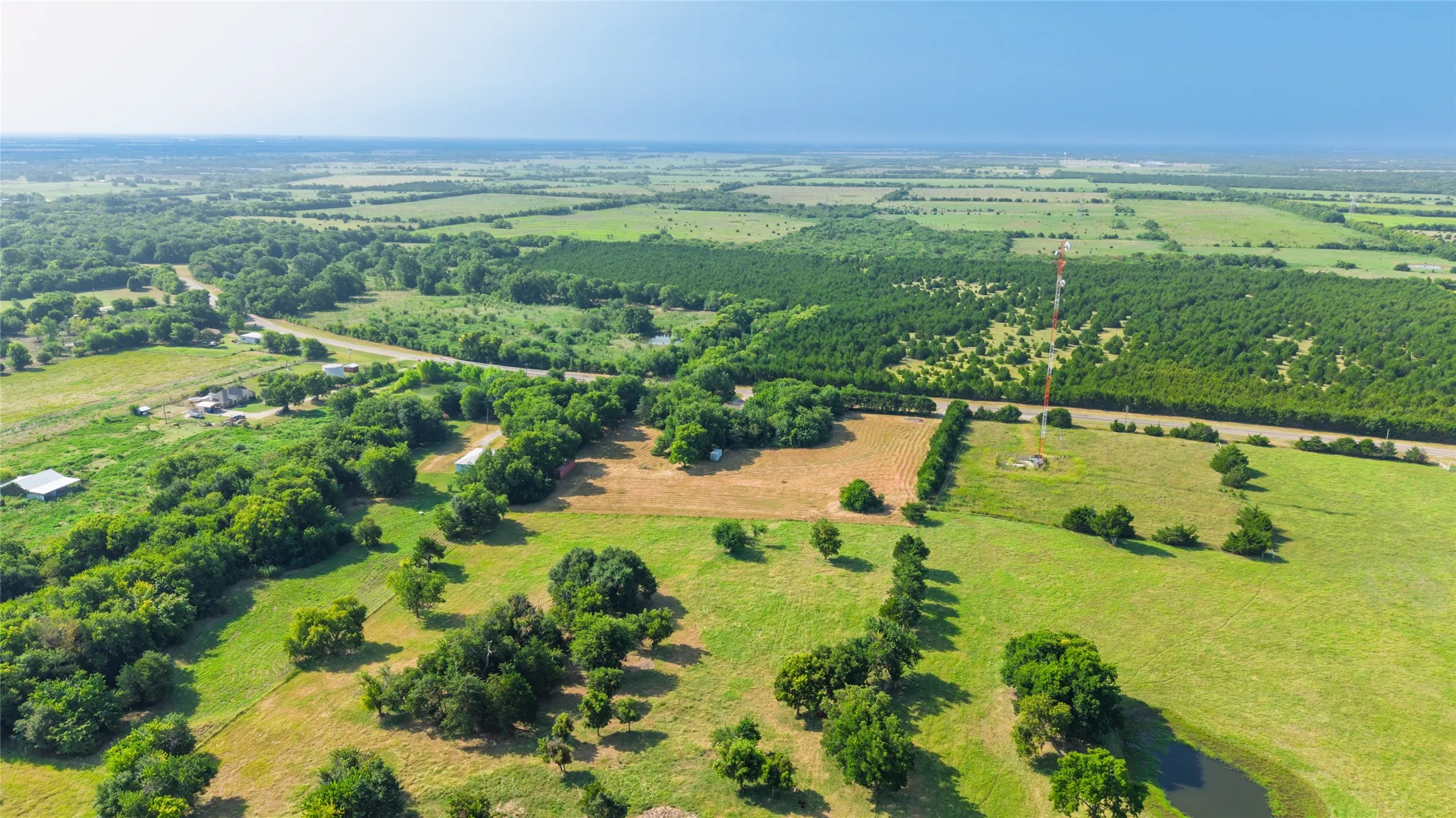 Expansive land parcel featuring open fields, mature tree lines, and a visible pond