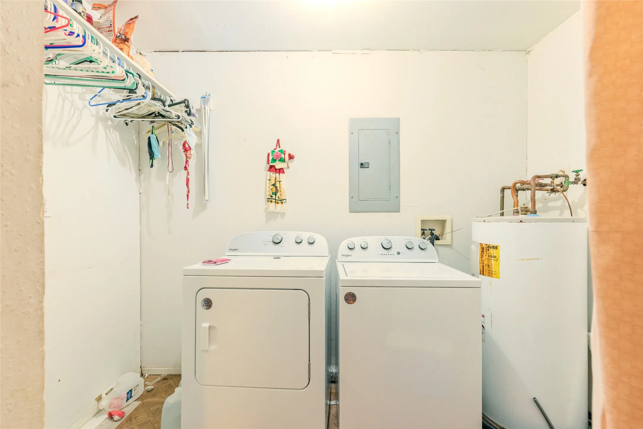 Dedicated laundry room featuring side-by-side washer and dryer units, wall-mounted sink with brass fixtures, abundant storage cabinetry, and built-in drying rack with multiple hooks for air-drying garments