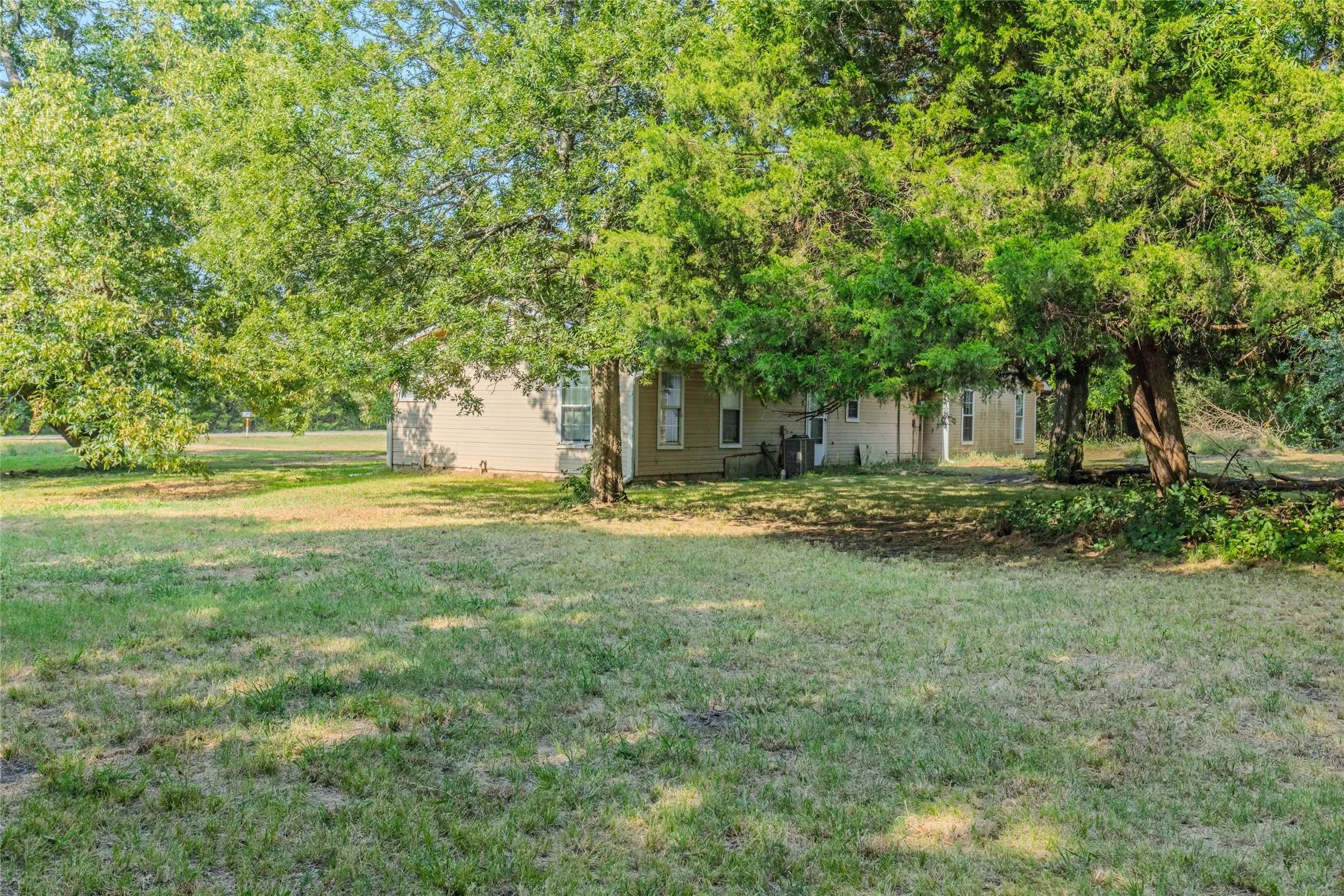 Expansive grounds featuring mature shade trees and a generous lawn, with a single-story residence set back from the property edge