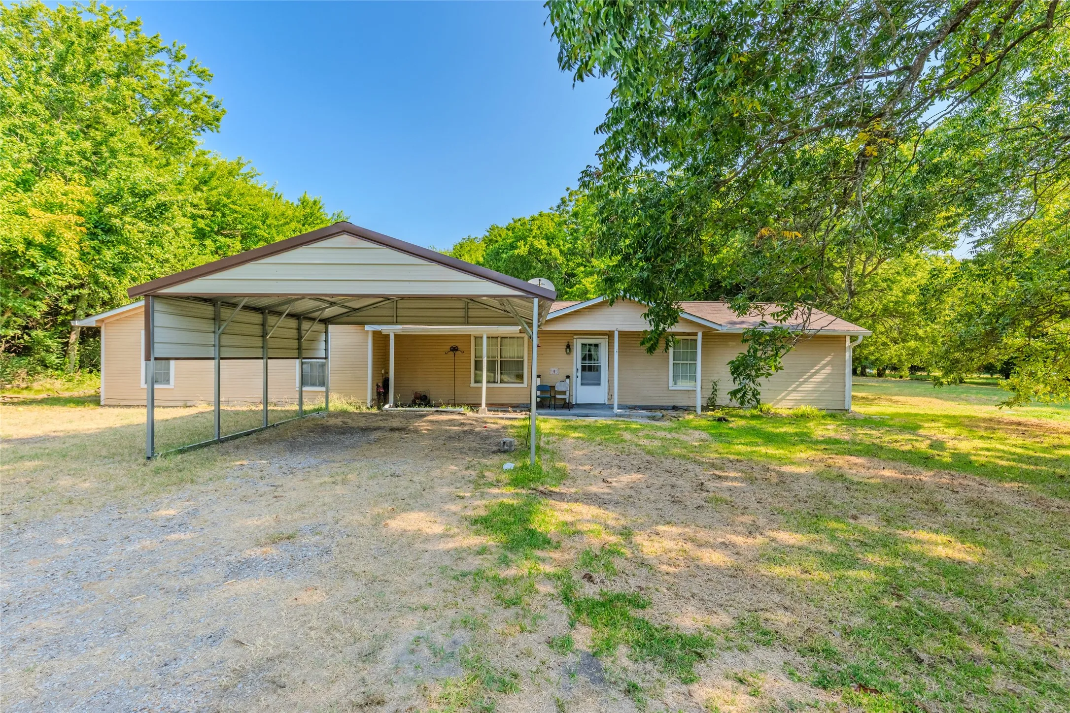Charming single-story residence featuring a covered carport with metal framing, brick exterior, and mature landscaping throughout the grounds