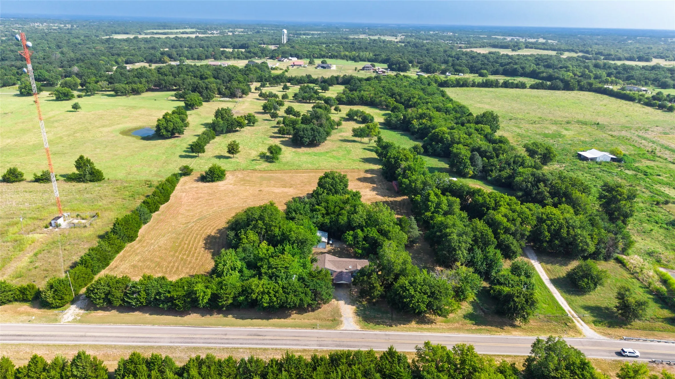 Sprawling rural acreage featuring mature tree clusters, open pastureland, and a residence situated on the property