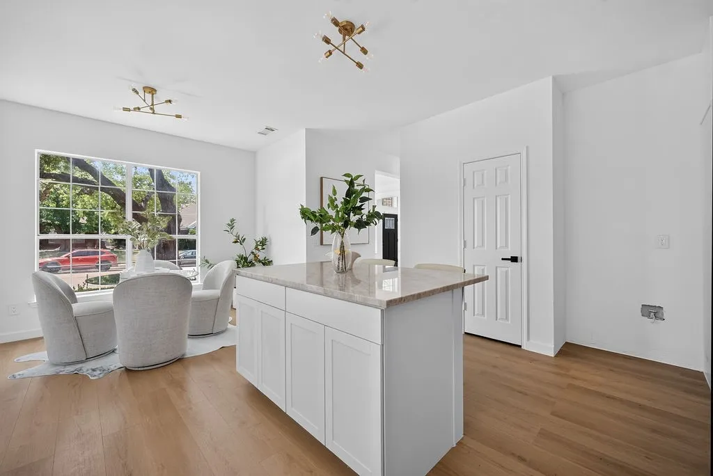 Open-concept kitchen and living area featuring a large island with wood-finish countertop and white cabinetry, abundant natural light from expansive multi-pane windows, warm wood-finish flooring throughout, and access to outdoor space