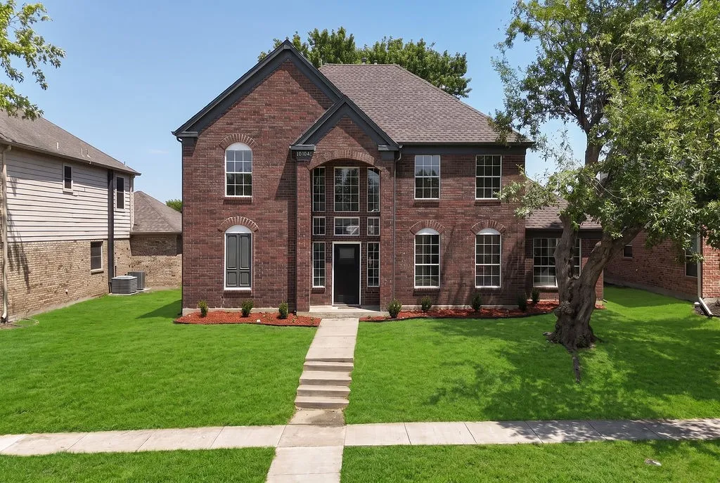 Elegant brick Colonial featuring a symmetrical facade with arched entryway, multiple windows with black trim, and a peaked roofline