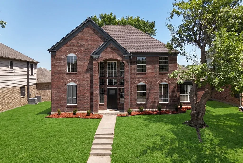 Stately two-story brick Colonial with symmetrical facade featuring multiple windows with black trim, arched entry vestibule, and pitched roof