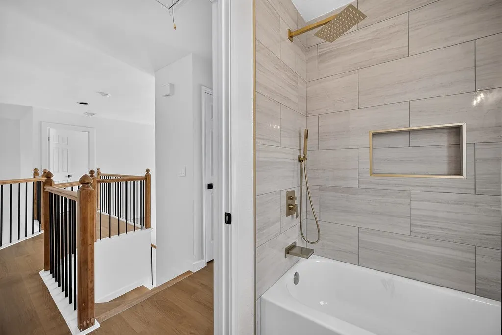 Primary Bathroom featuring a frameless glass-enclosed shower with linear tile surround, white subway tile walls, integrated niche shelving, brushed brass showerhead and handheld fixture, and a soaking tub with deck-mounted controls