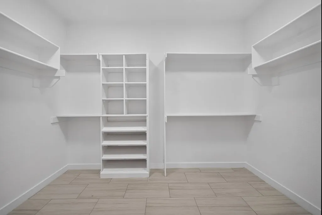 Built-in shelving with cubby storage, multiple hanging rods, and light-toned tile flooring