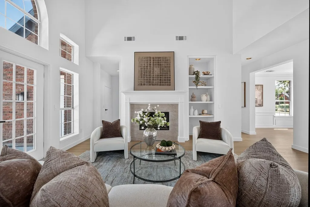 Bright, open living area featuring high ceilings, abundant natural light from multi-pane windows, and a fireplace with built-in shelving