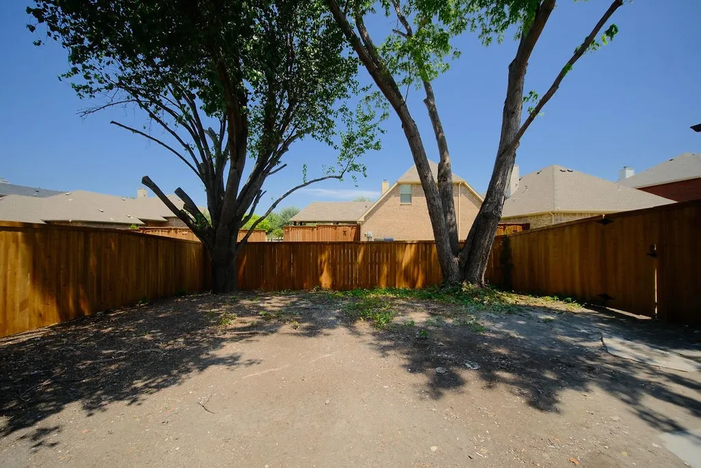 Spacious backyard retreat featuring mature shade trees, wooden perimeter fencing, and a generously sized dirt and gravel surface ideal for customization