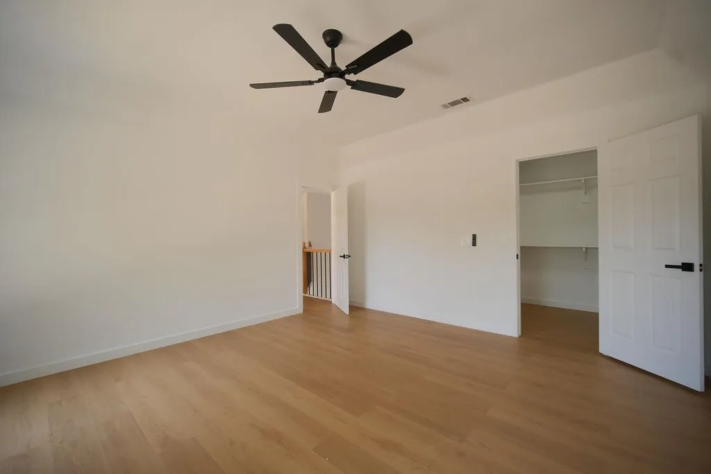 Spacious primary bedroom with wood-finish flooring, ceiling fan with dark metal blades, and dual closet access