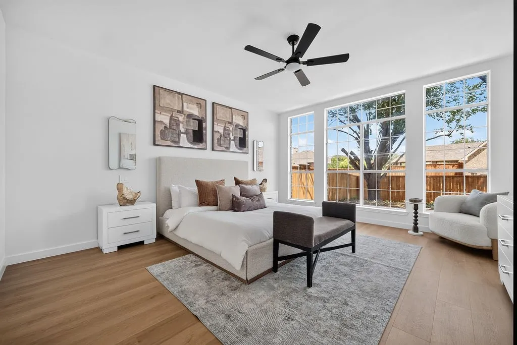 Bright primary bedroom with hardwood flooring, abundant natural light from multiple glass doors opening to an outdoor space, ceiling fan, and ensuite access