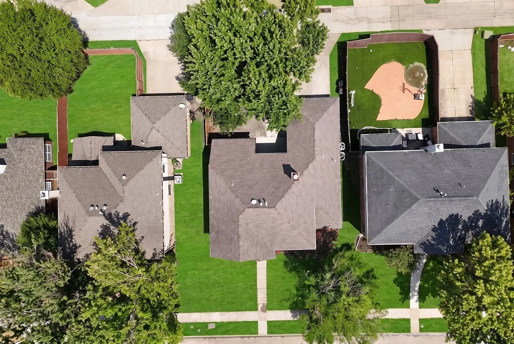 Aerial view showcasing three residences with individual asphalt roofing, manicured lawns, mature landscaping, and defined hardscaped driveways