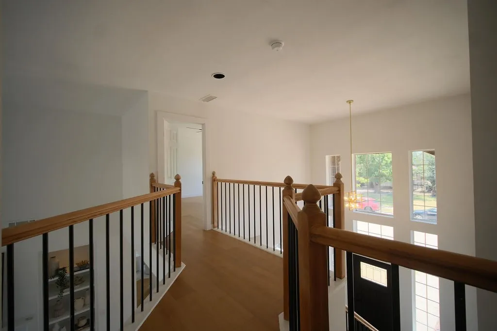 Elegant upper-level hallway featuring warm wood-finish flooring, wood railings with metal balusters, and abundant natural light from multiple glass doors and windows
