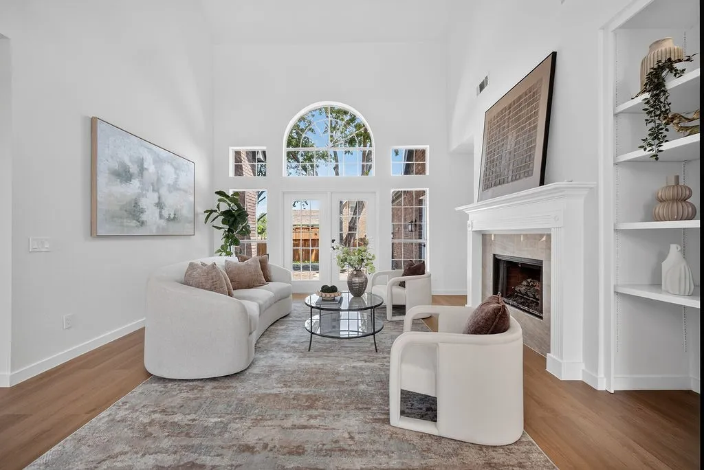 Bright, light-filled living room showcasing soaring ceilings with a circular transom window, hardwood flooring, and a gas fireplace with built-in shelving