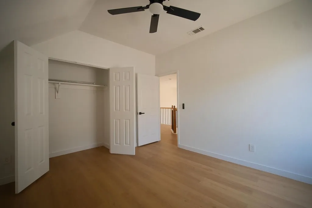 Spacious bedroom offering wood-finish flooring, a ceiling fan, and a generous walk-in closet with shelving and hanging rod