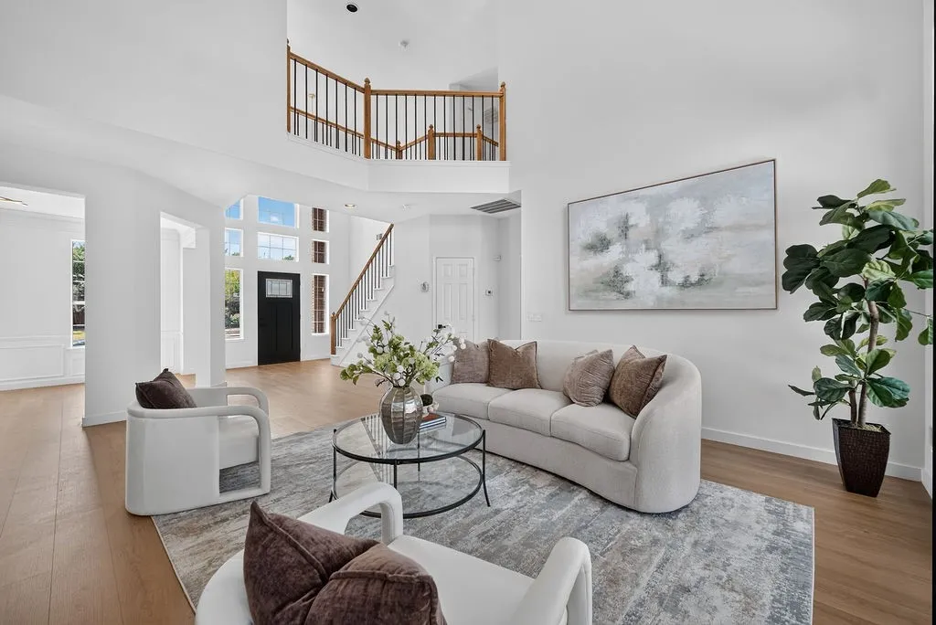 Bright, open living area showcasing a curved sectional sofa, glass-top coffee table, and light wood-finish flooring throughout