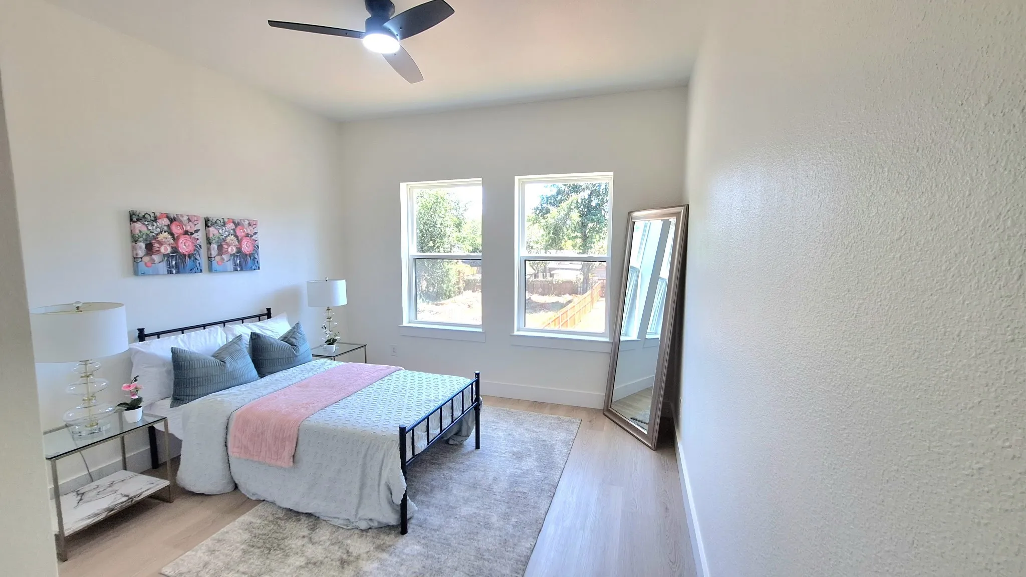 Light wood-finish flooring, a contemporary ceiling fan, and two windows with white trim